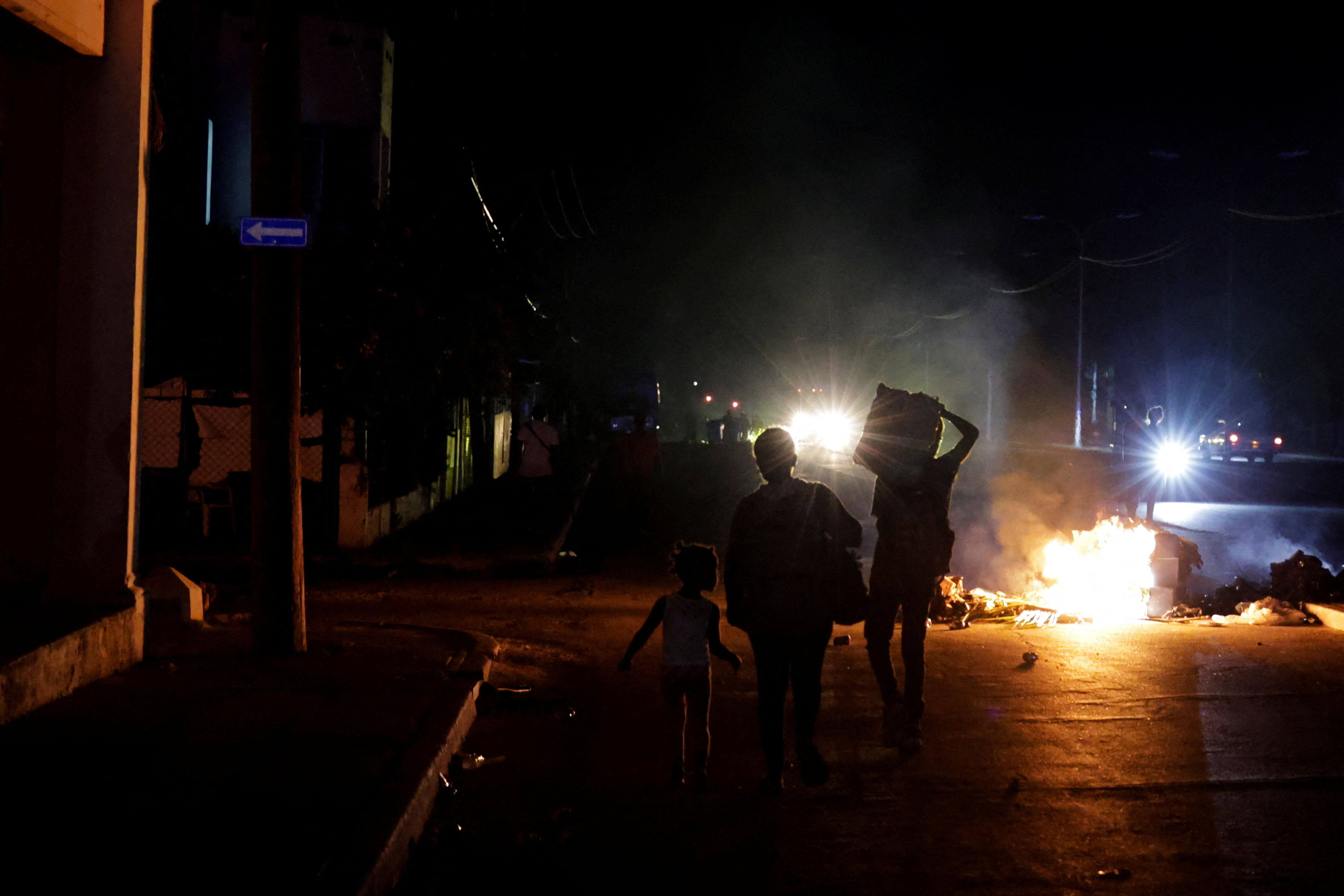 People walk past trash set on fire in the middle of a street during a protest against frequent power cuts as Havana faces its worst rolling blackouts in decades amid a U.S. blockade