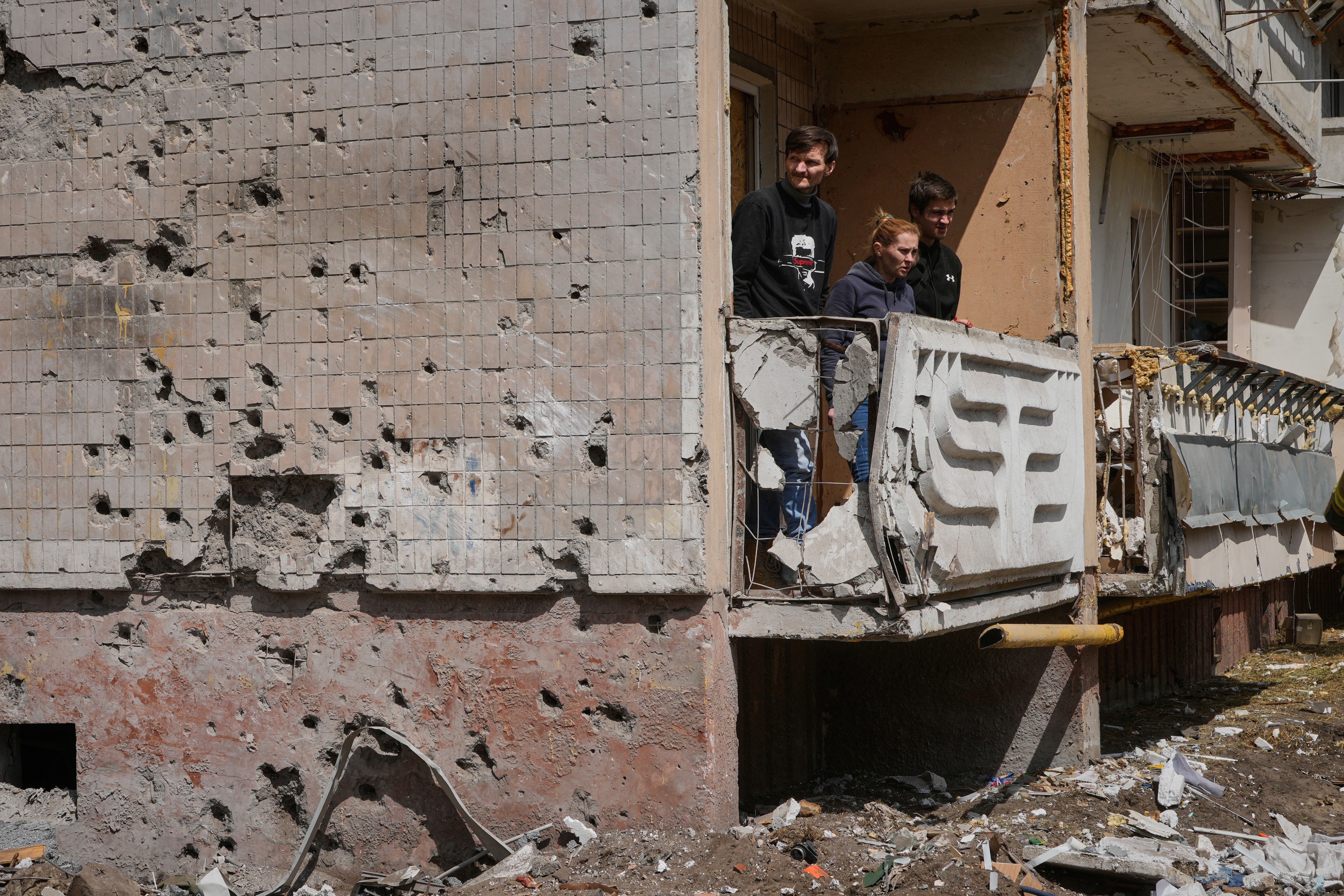 Residents of a neighbouring house, whose wall is damaged with shrapnel, look at the site of a Russian missile strike that hit an apartment house on Thursday