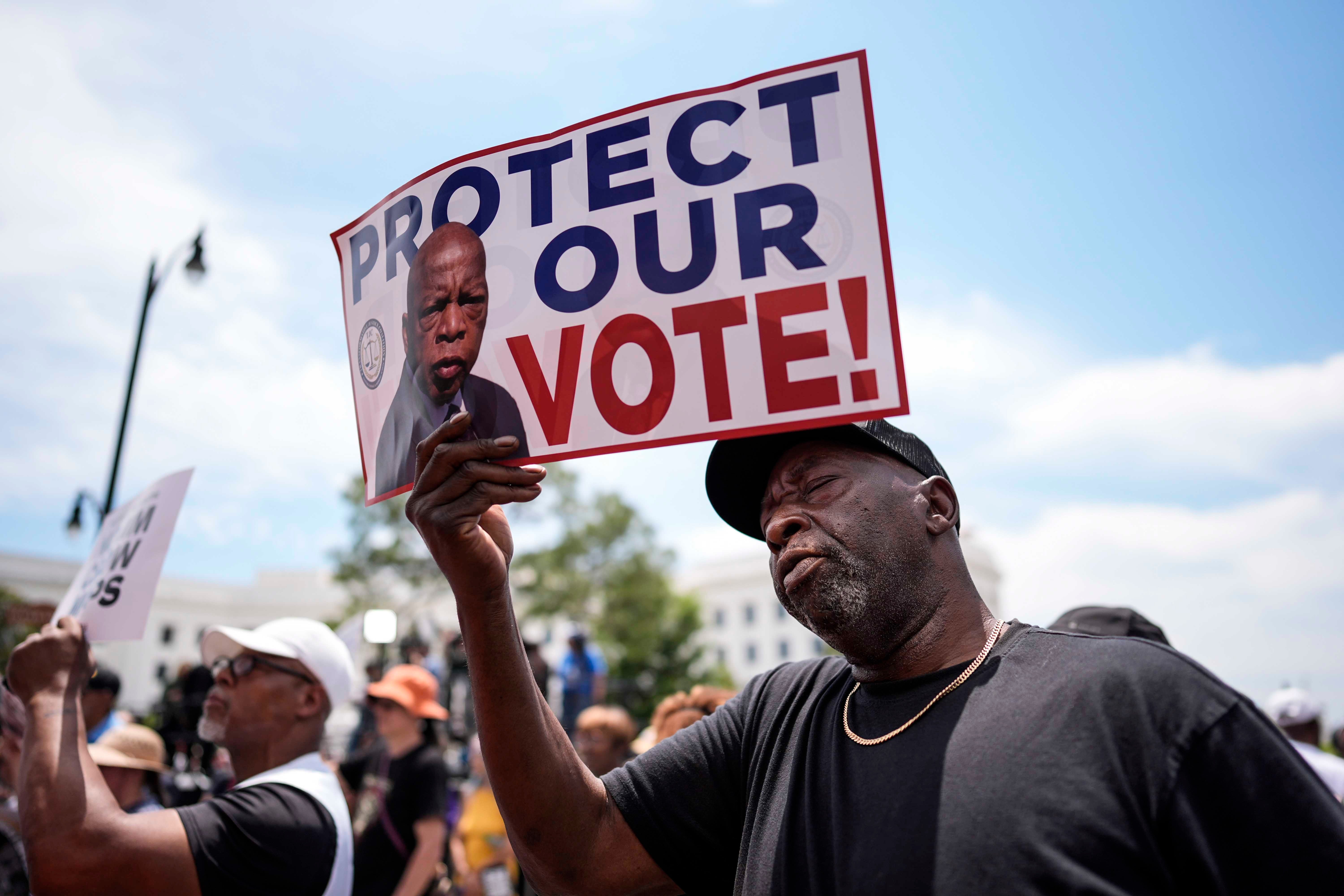 Rally-goer Aaron McGuire holds a poster with the image of the late Rep. John Lewis, the influential civil rights activist who led a march from Selma to Montgomery in 1965