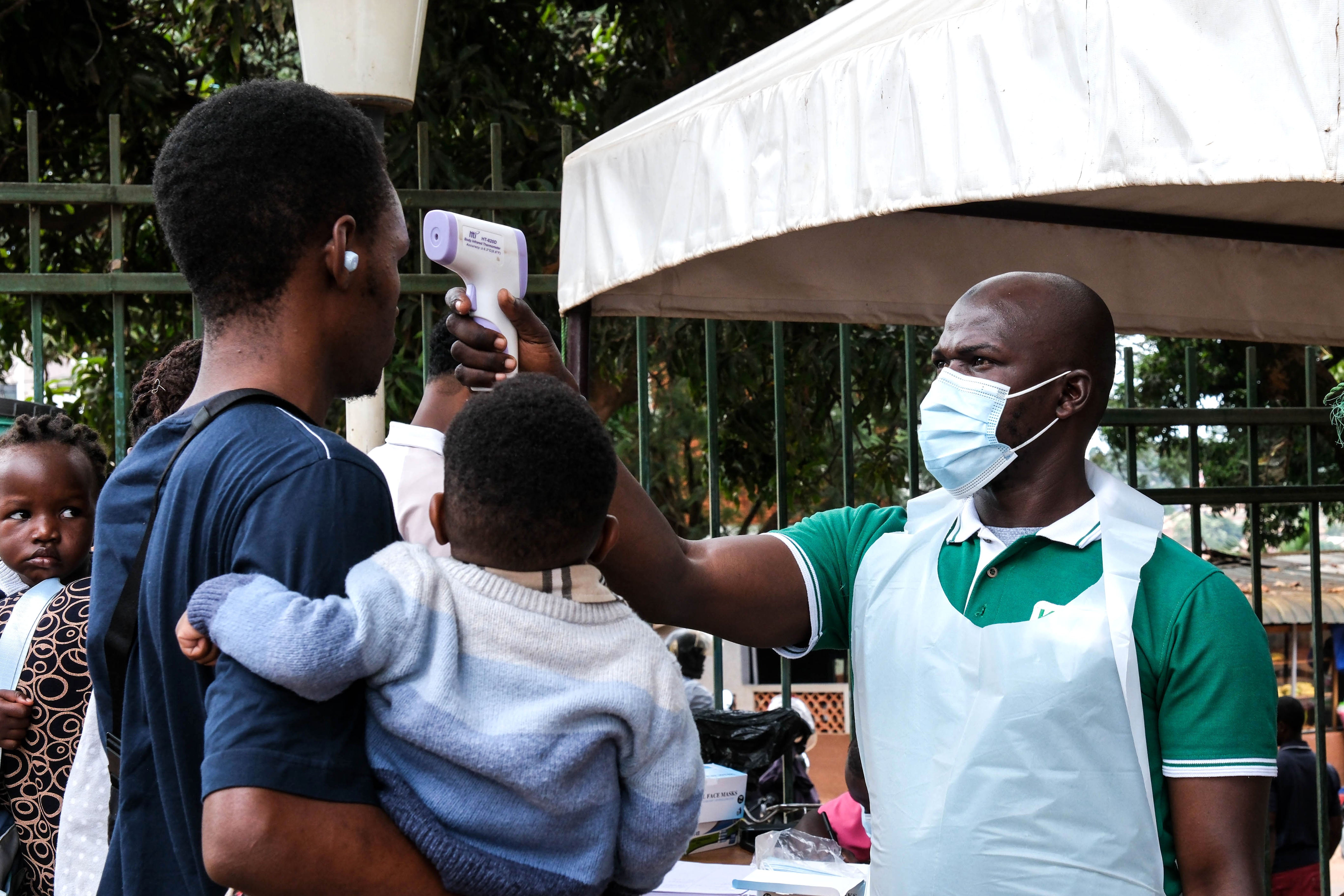 A health official uses a thermometer to screen people in front of Kibuli Muslim Hospital in Kampala, Uganda