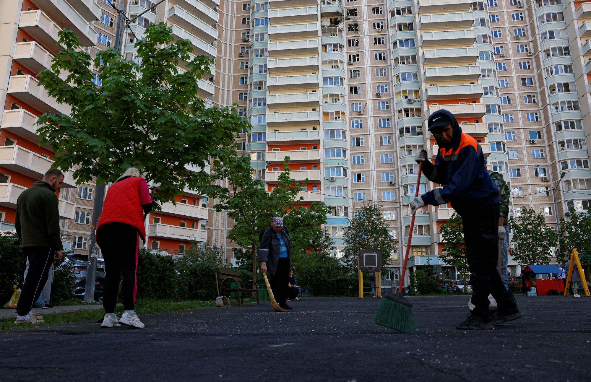 Municipal workers sweep up broken glass in front of a damaged apartment building following a Ukrainian drone attack