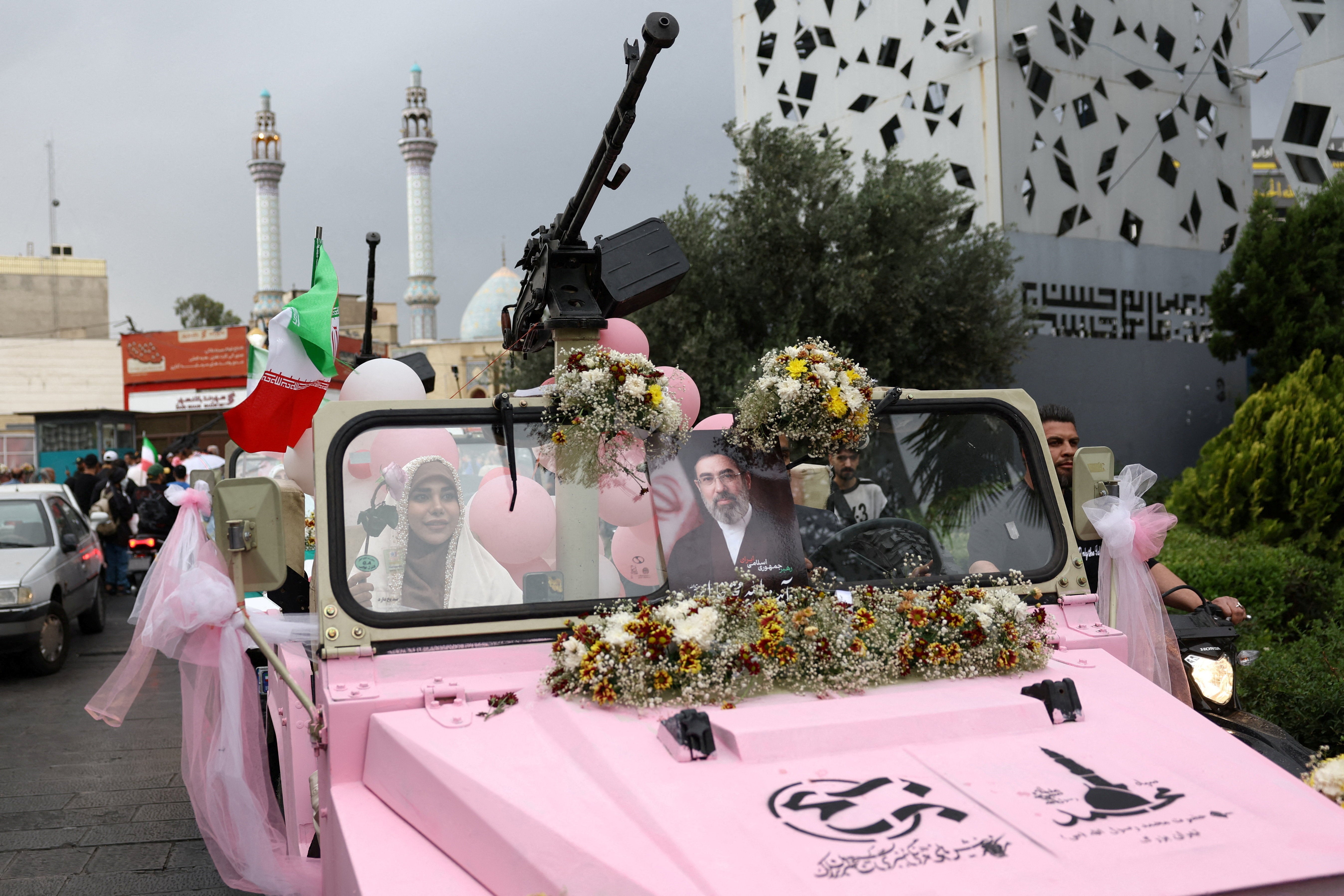 An Iranian couple arrive on a military vehicle during a public wedding ceremony called 