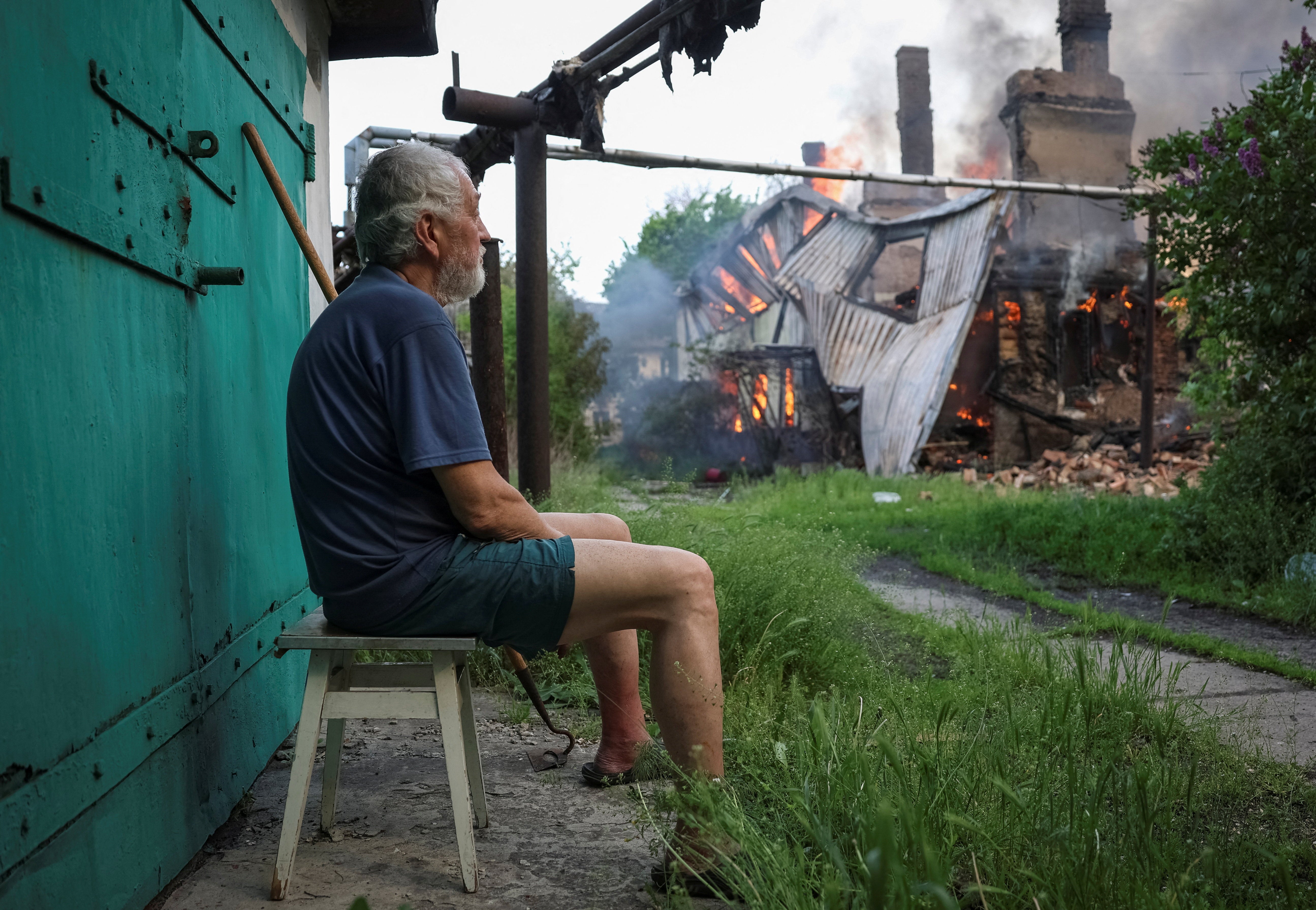 A resident sits near a burning house hit by Russian drone in the frontline city of Bilozerske in Donetsk region (Reuters)