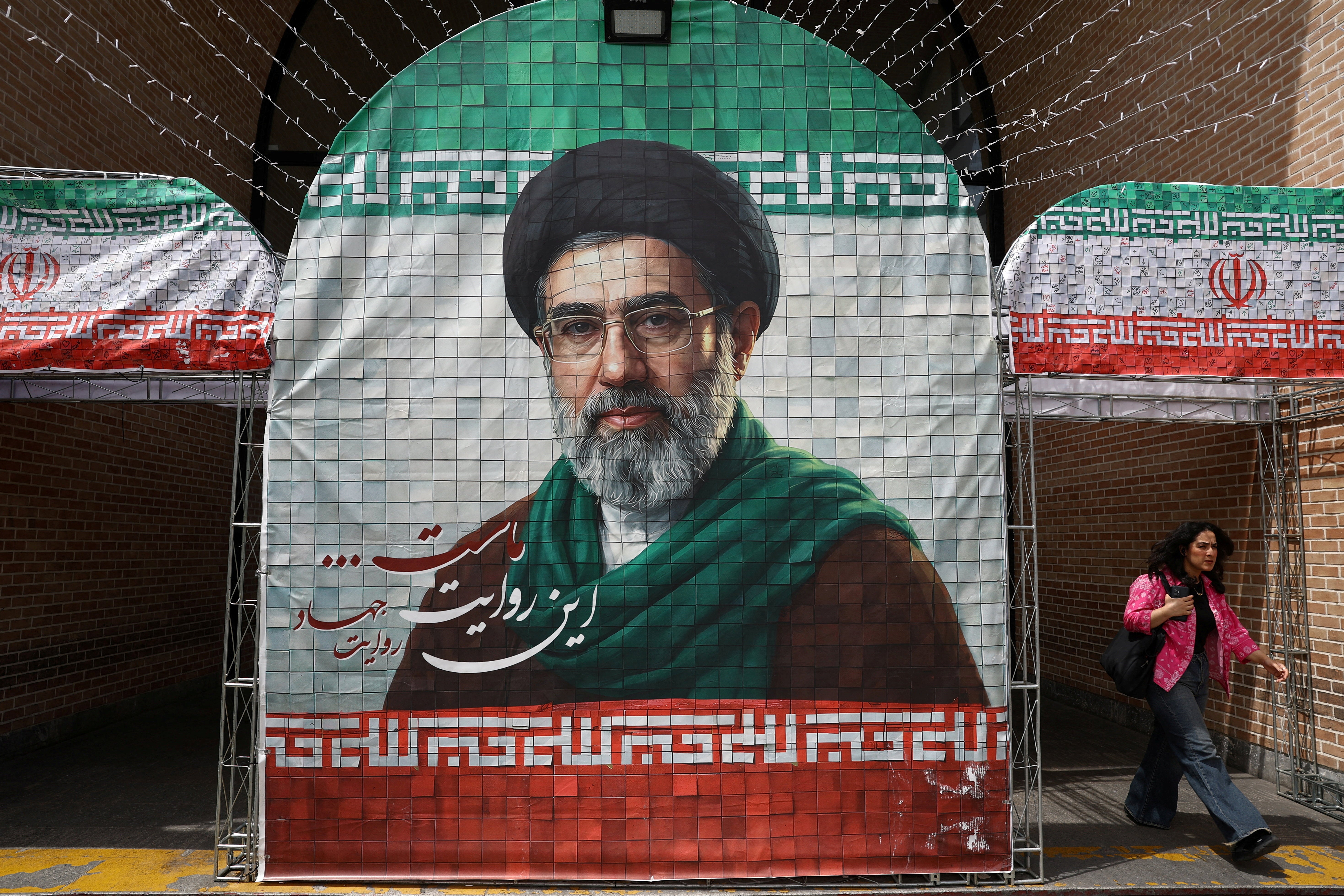 A woman walks next to a banner with a picture of Iran's new Supreme Leader Mojtaba Khamenei in Tehran (Reuters)