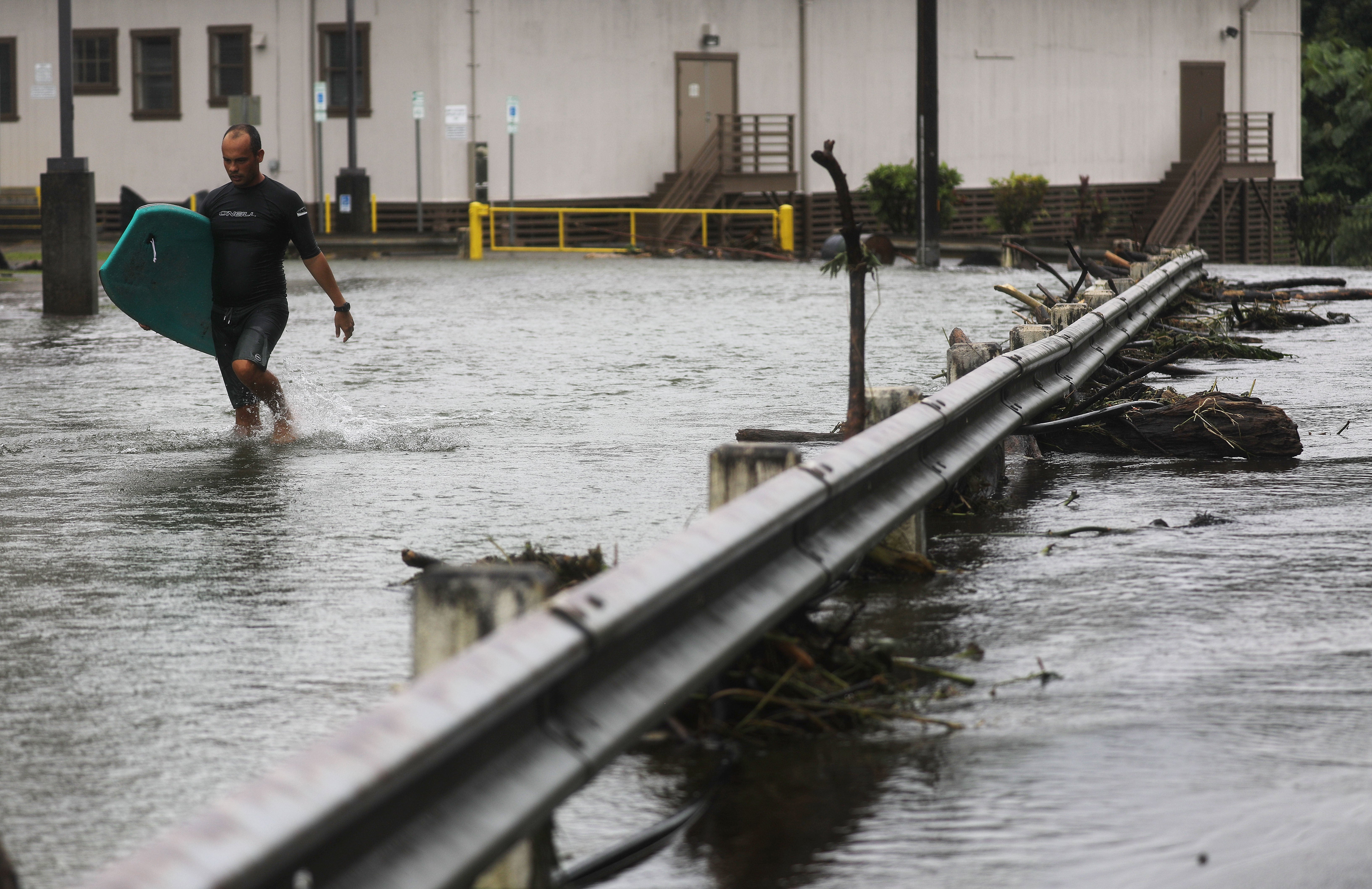 A resident carries his bodyboard through floodwaters after Tropical Storm Lane hit the Big Island in August 2018. Flooding and winds have devastated the Hawaiian islands in recent years