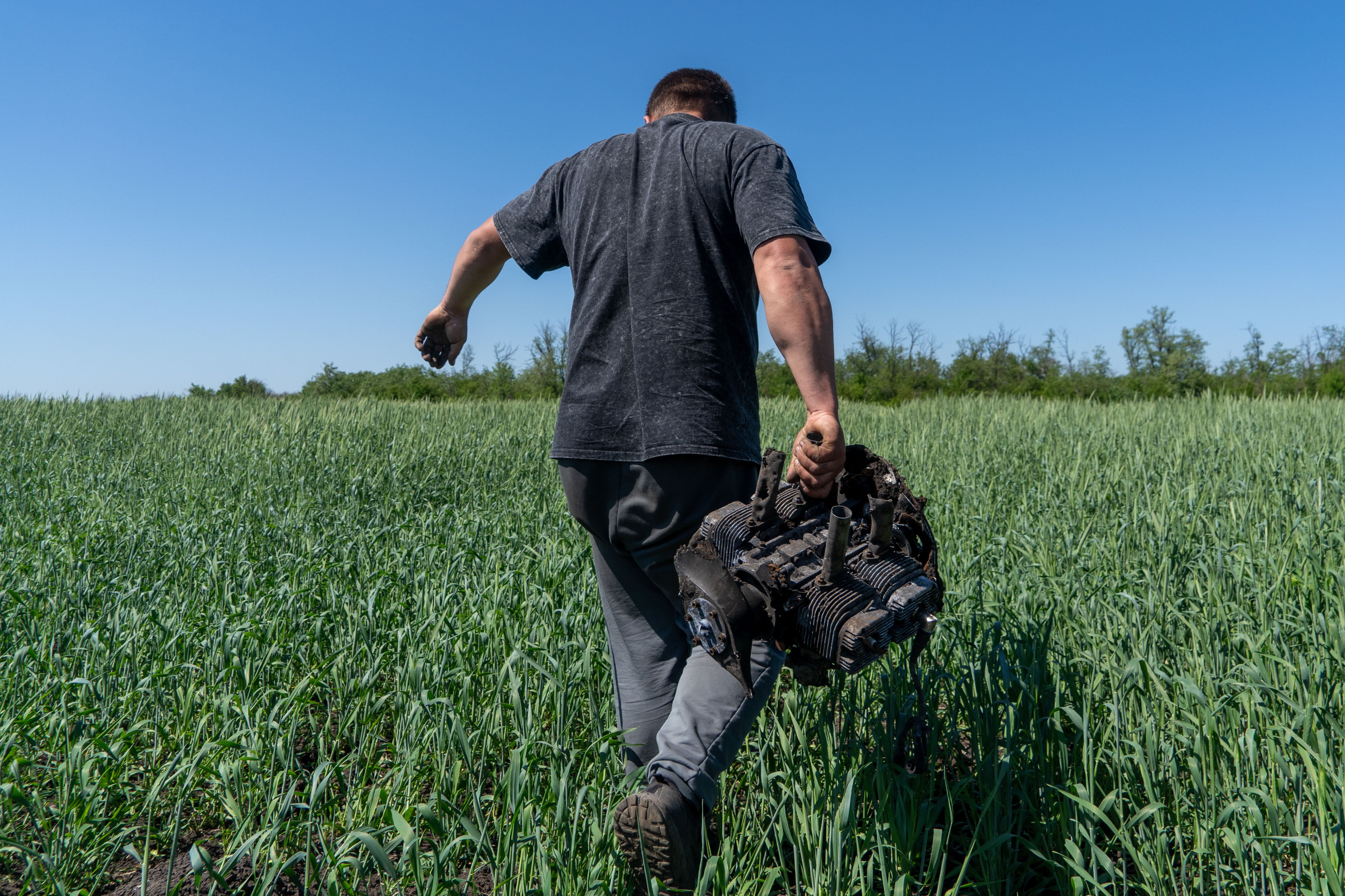 A farmer carries a fragment of a Russian drone on an agricultural field near the front line in the Kharkiv region, Ukraine, Friday, May 22, 2026