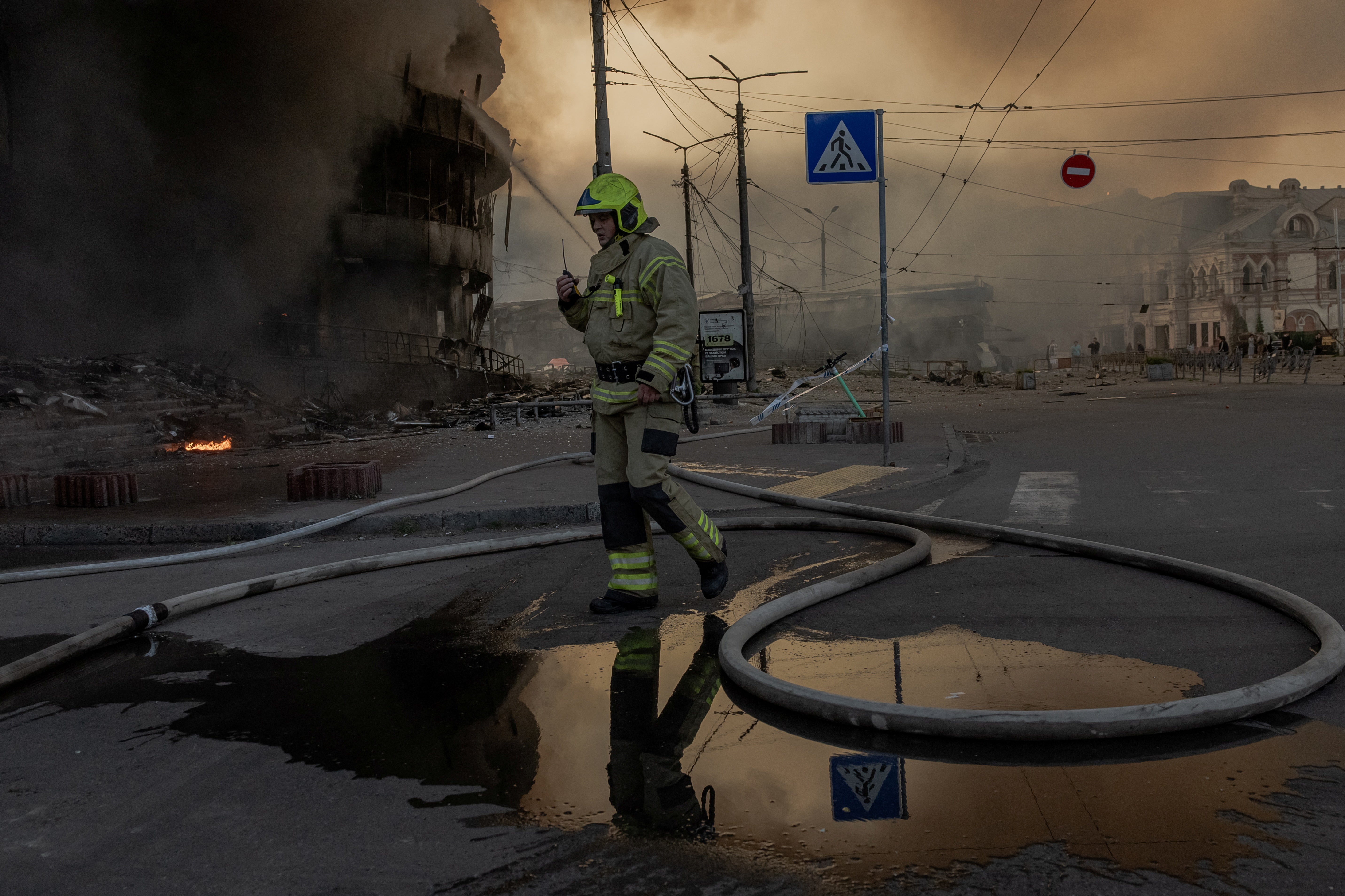 A Ukrainian firefighter operates at the site of a heavily damaged shopping centre as smoke rises in the background