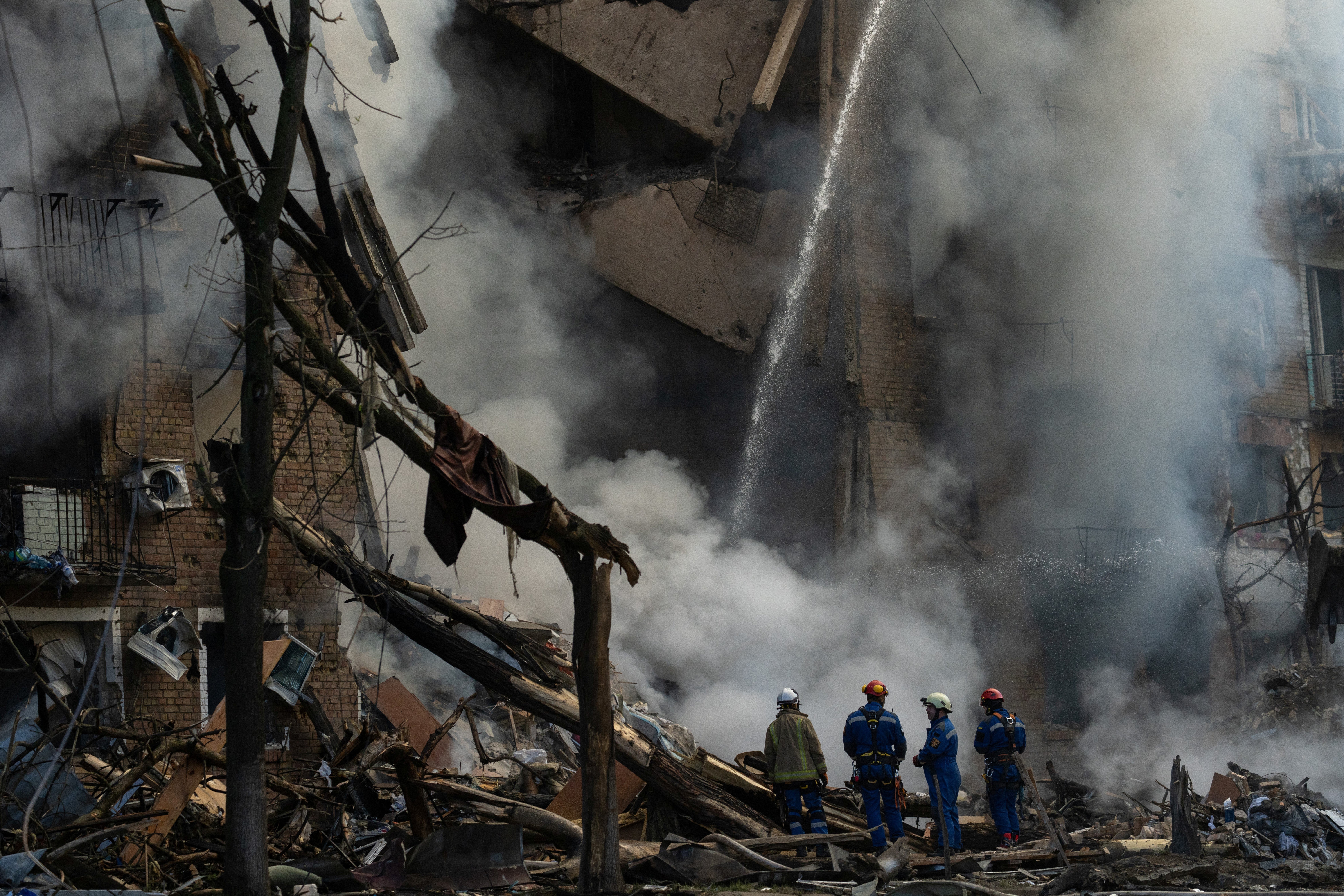 Rescuers operate at the site of a heavily damaged building as smoke rises following Russian strikes in Kyiv