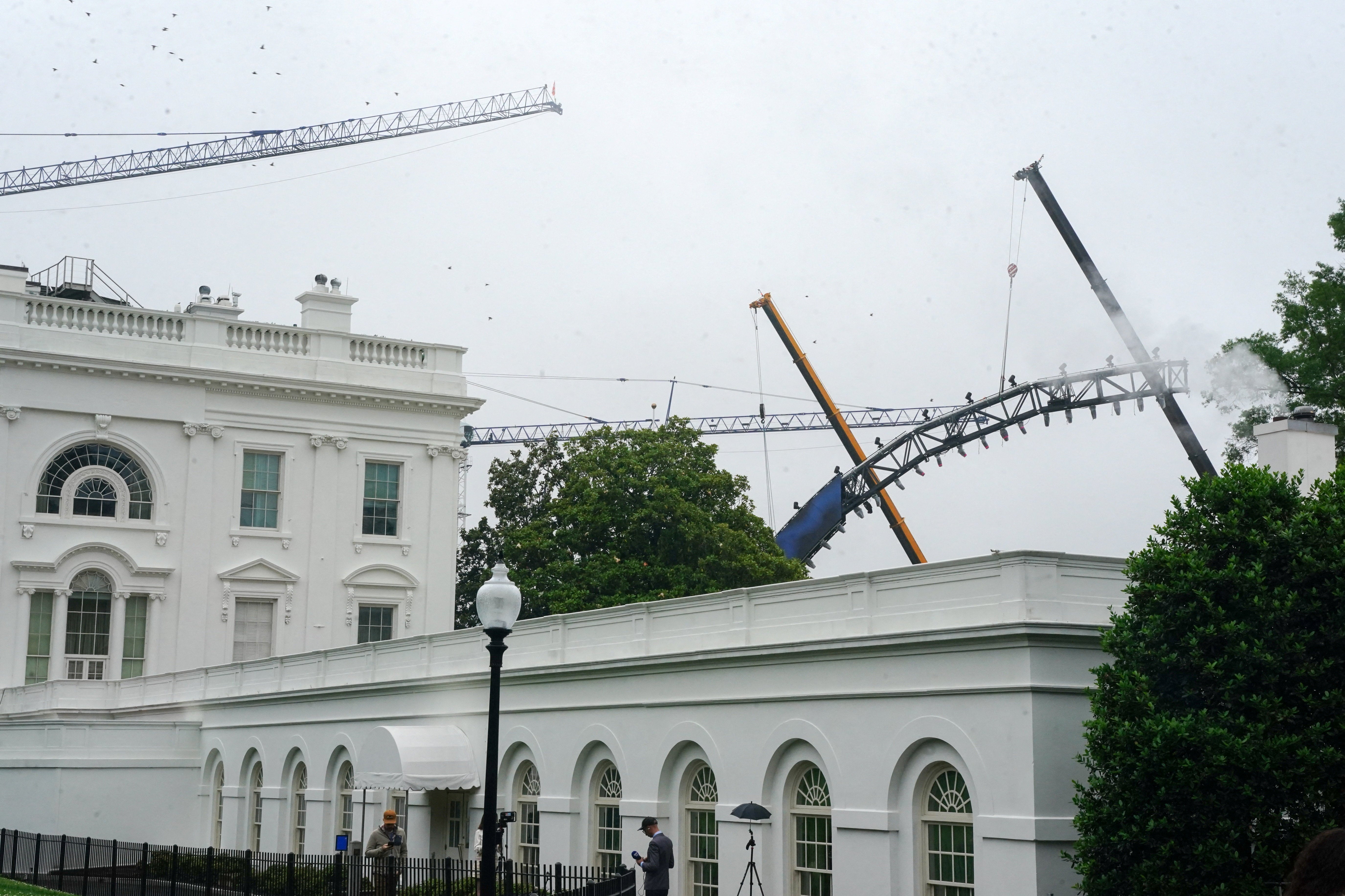 In one photo taken Monday, cranes can be seen carrying a section of the rig as it arches in front of the White House