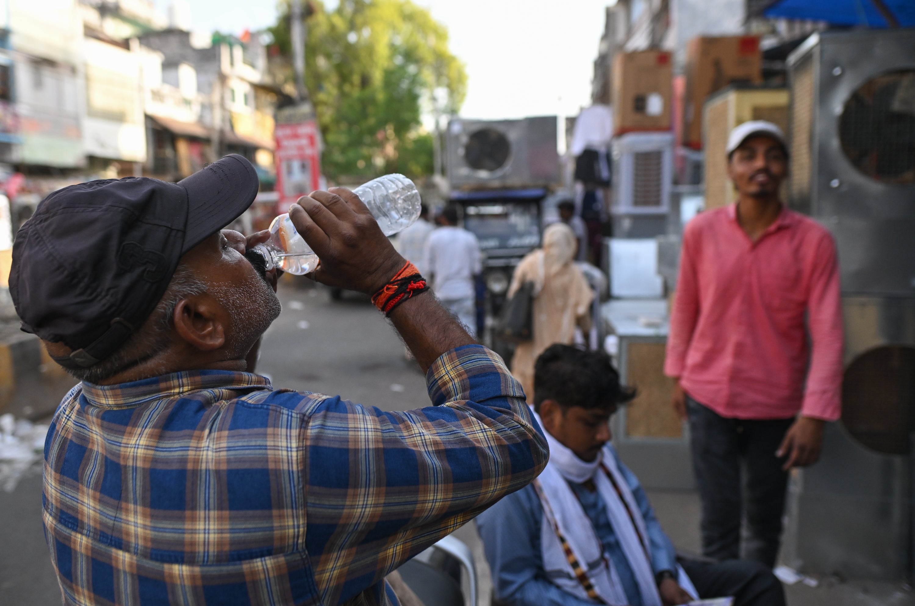 A man drinks water at a market selling air coolers and cooling appliances during hot weather conditions