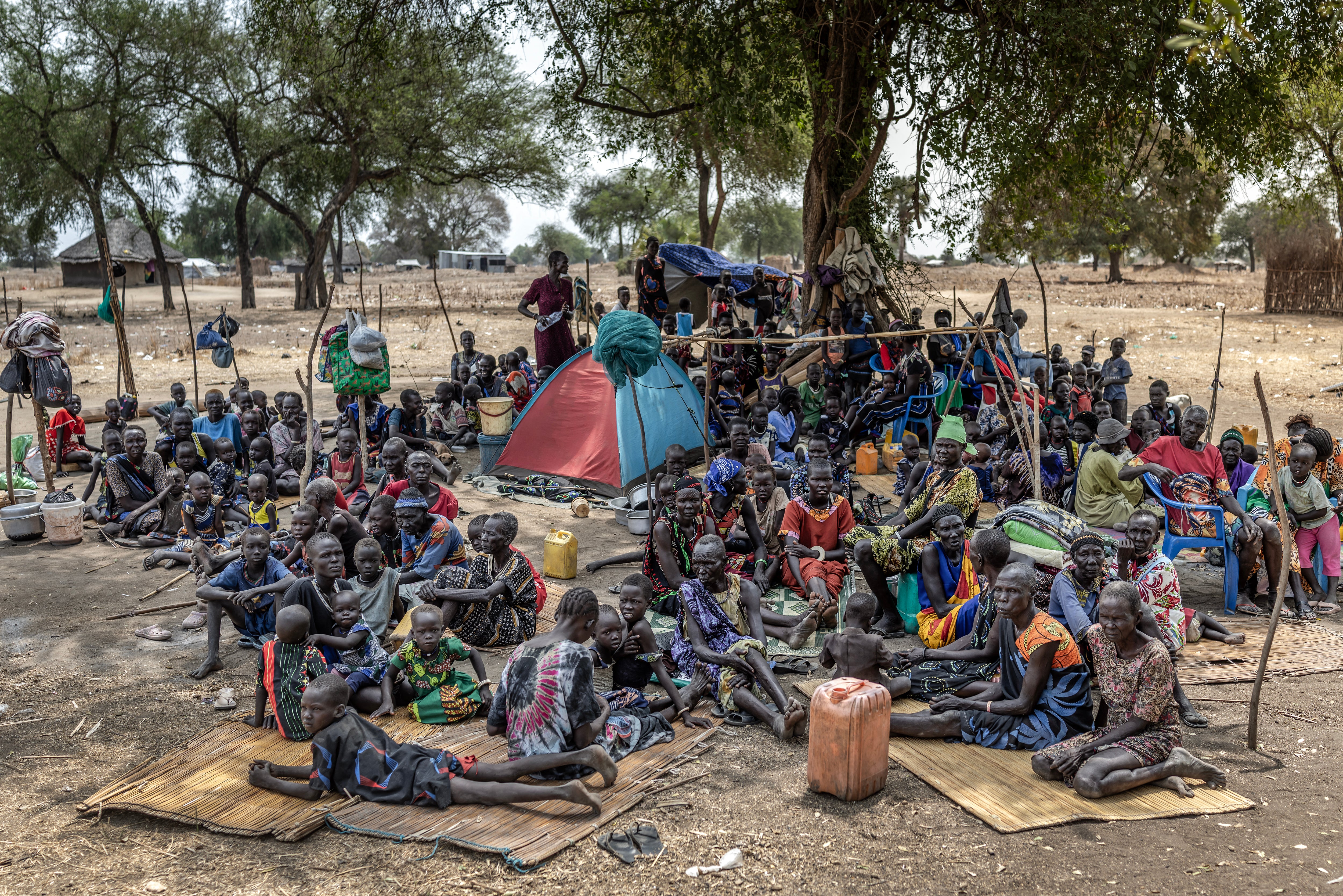 Families gather under the shade of a tree at an informal displacement site