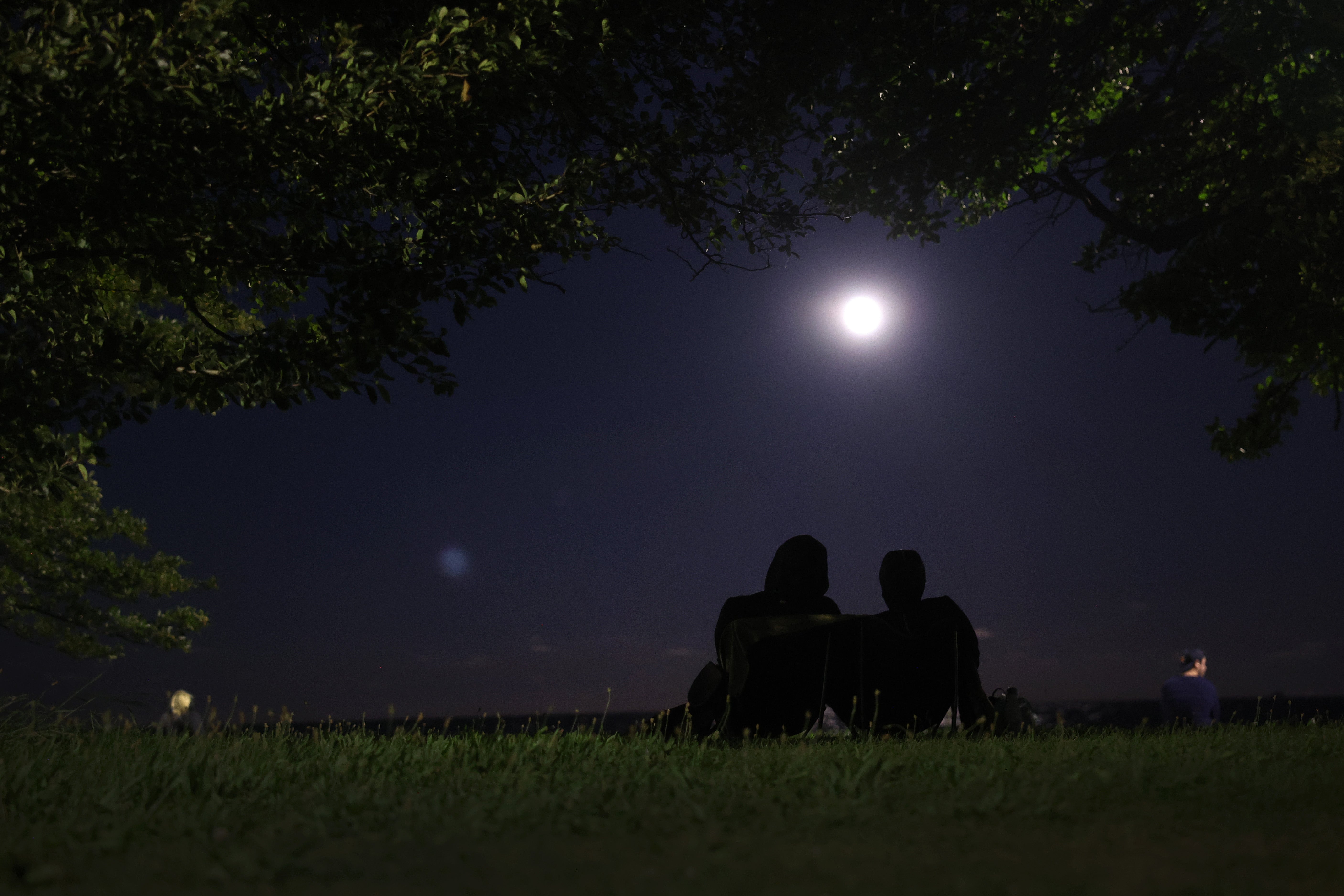 Two people watch the August 2023 blue moon rise in Chicago, Illinois. People should avoid light pollution for the clearest view of the night sky