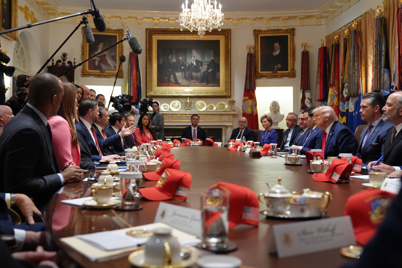 Cabinet officials seated around a White House table with red America 250 hats placed in front of them