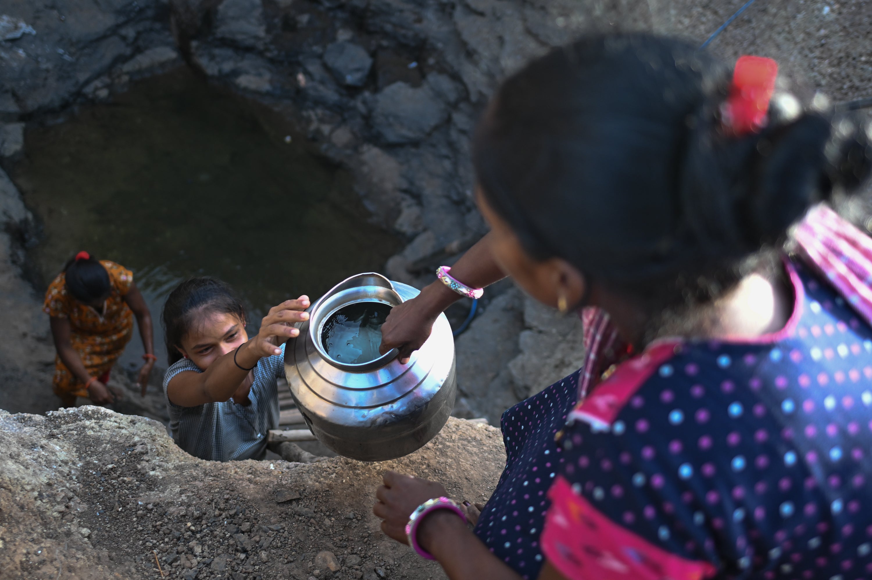 Women collect water from the partially dried remains of a well in a drought affected village on May 27, 2026 in Kaprada taluka of Valsad district, Gujarat, India