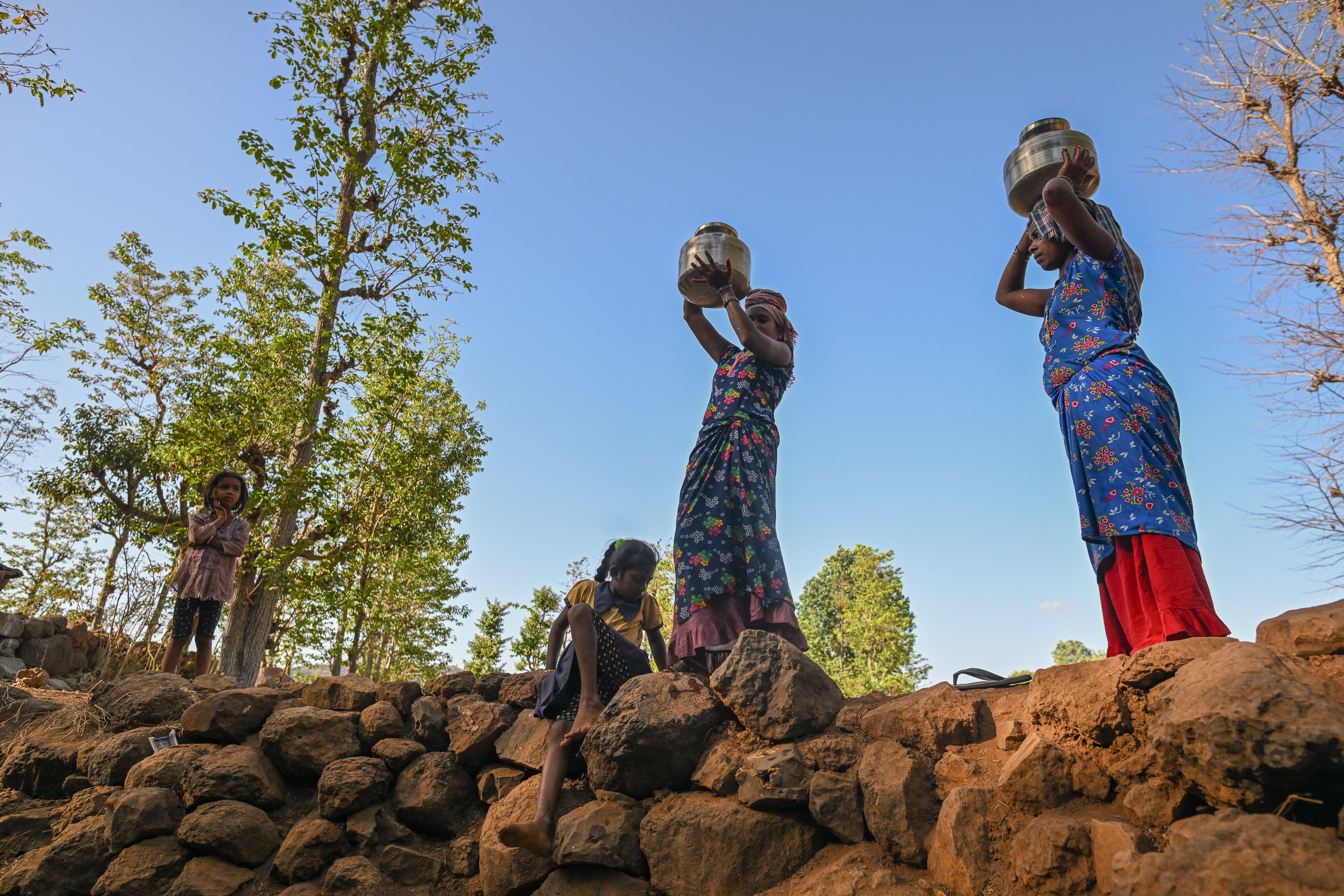 Women carry containers after collecting water from the stagnant and polluted remains of a partially dried well in a drought affected village