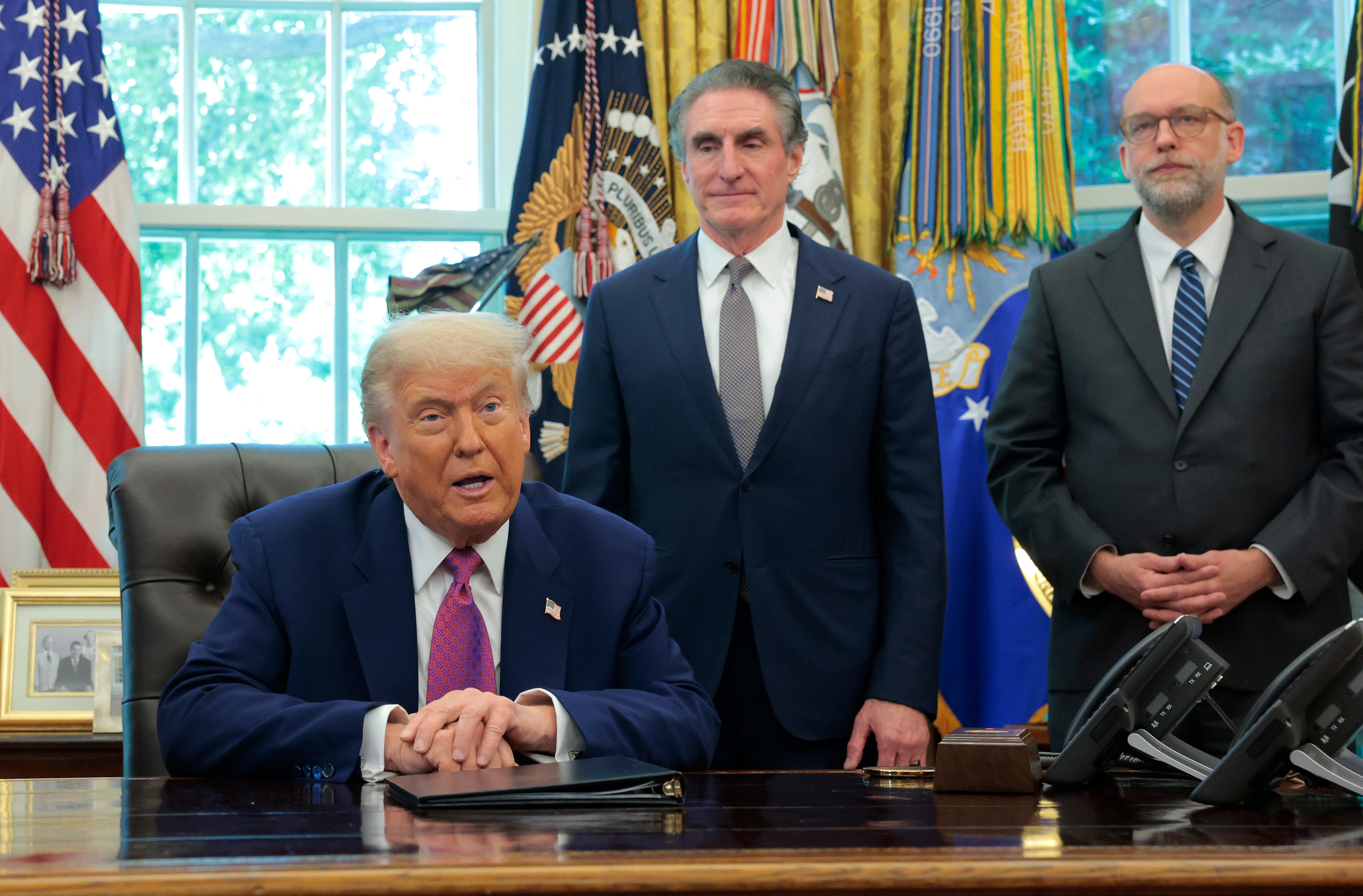 Budget director and Project 2025 co-author Russell Vought (right) and Interior Secretary Doug Burgum stand behind President Donald Trump in the Oval Office of the White House