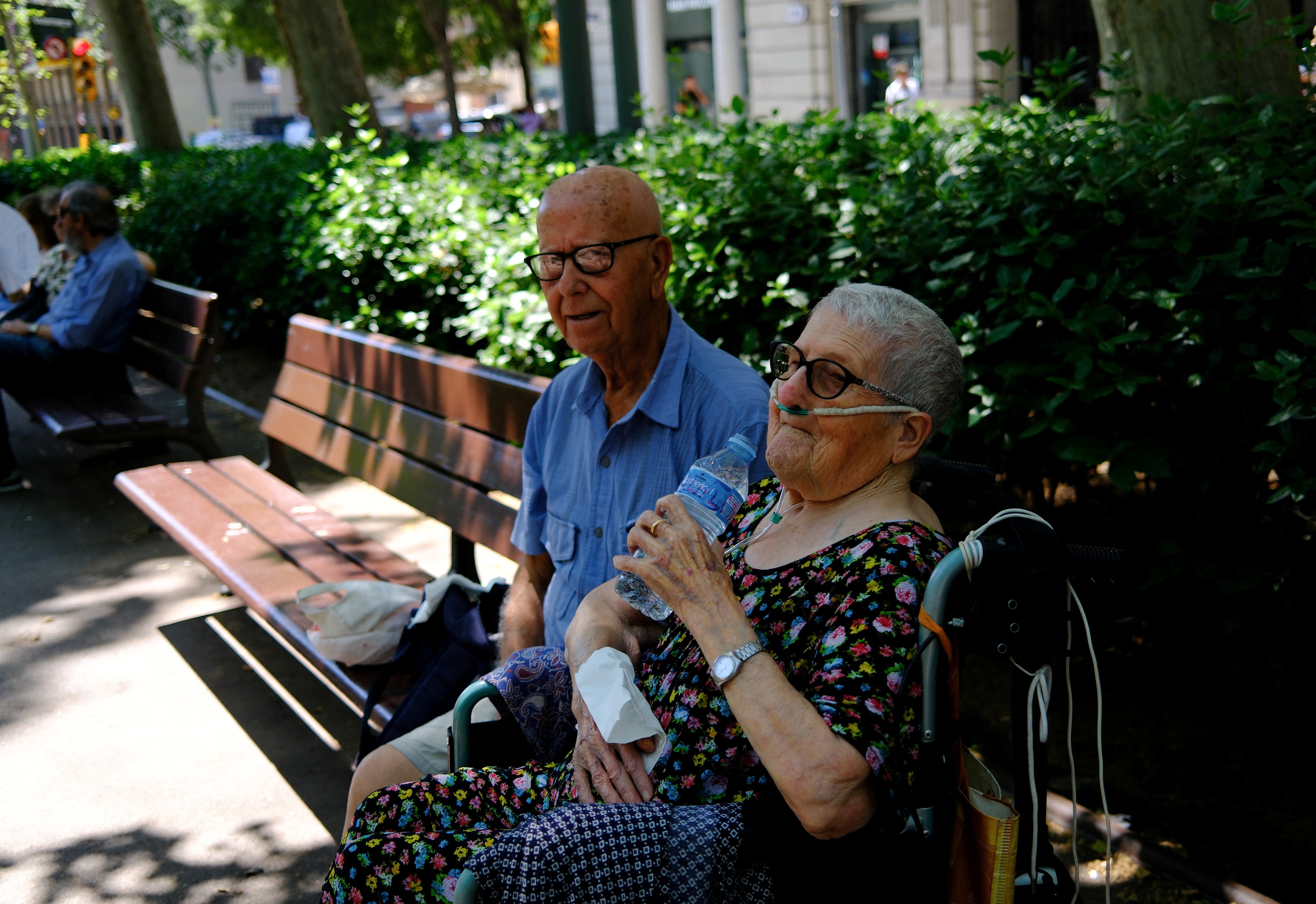 Aquilina, 89, who has respiratory problems, drinks water next to her husband, Antonio, 90, as they sit on a bench in the shade on Passeig de Sant Joan during a spring heatwave, in Barcelona, 29 May