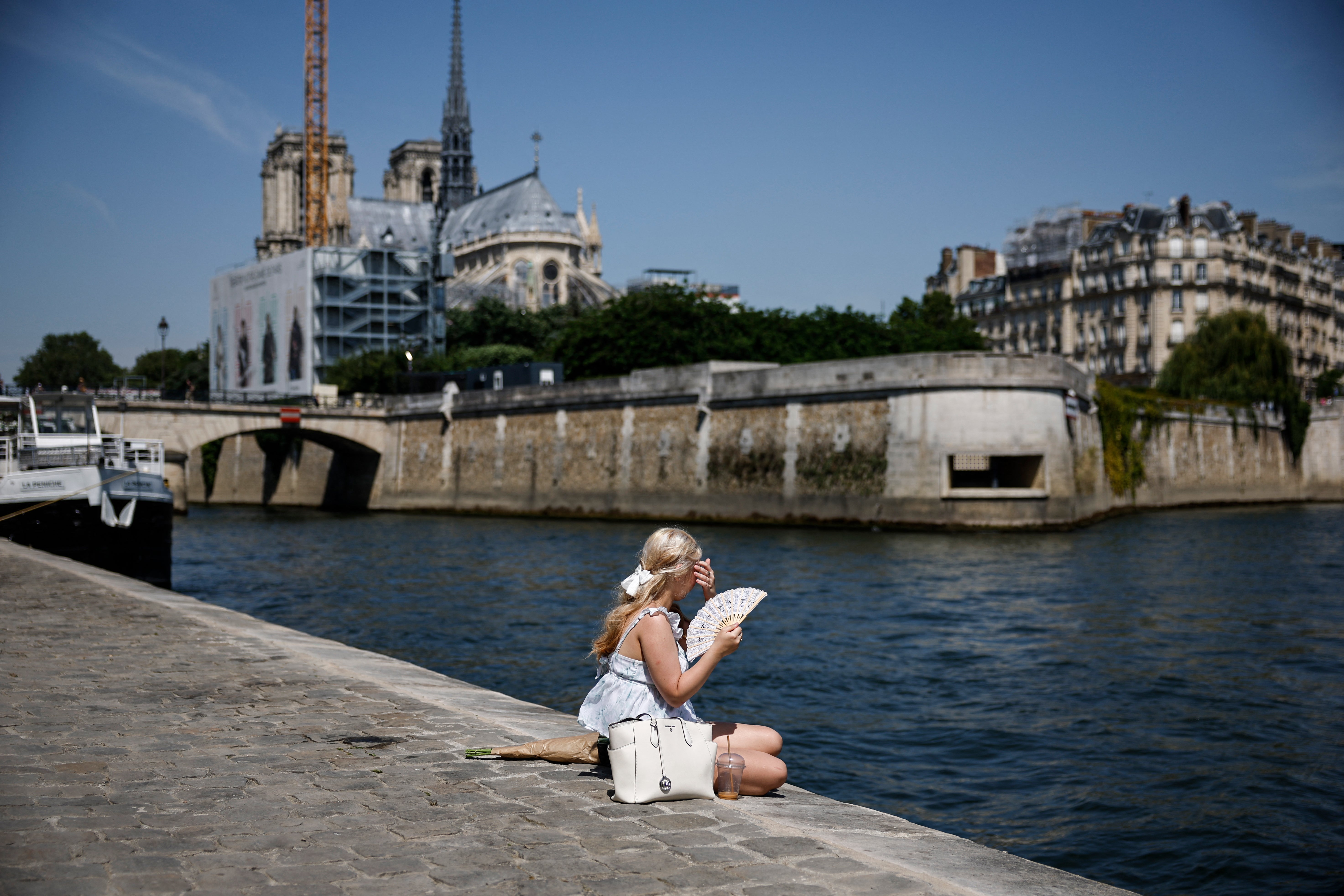 A woman sits on the Seine river banks behind the Notre-Dame Cathedral in Paris as a record-breaking early heatwave scorches a swathe of western Europe on May 28