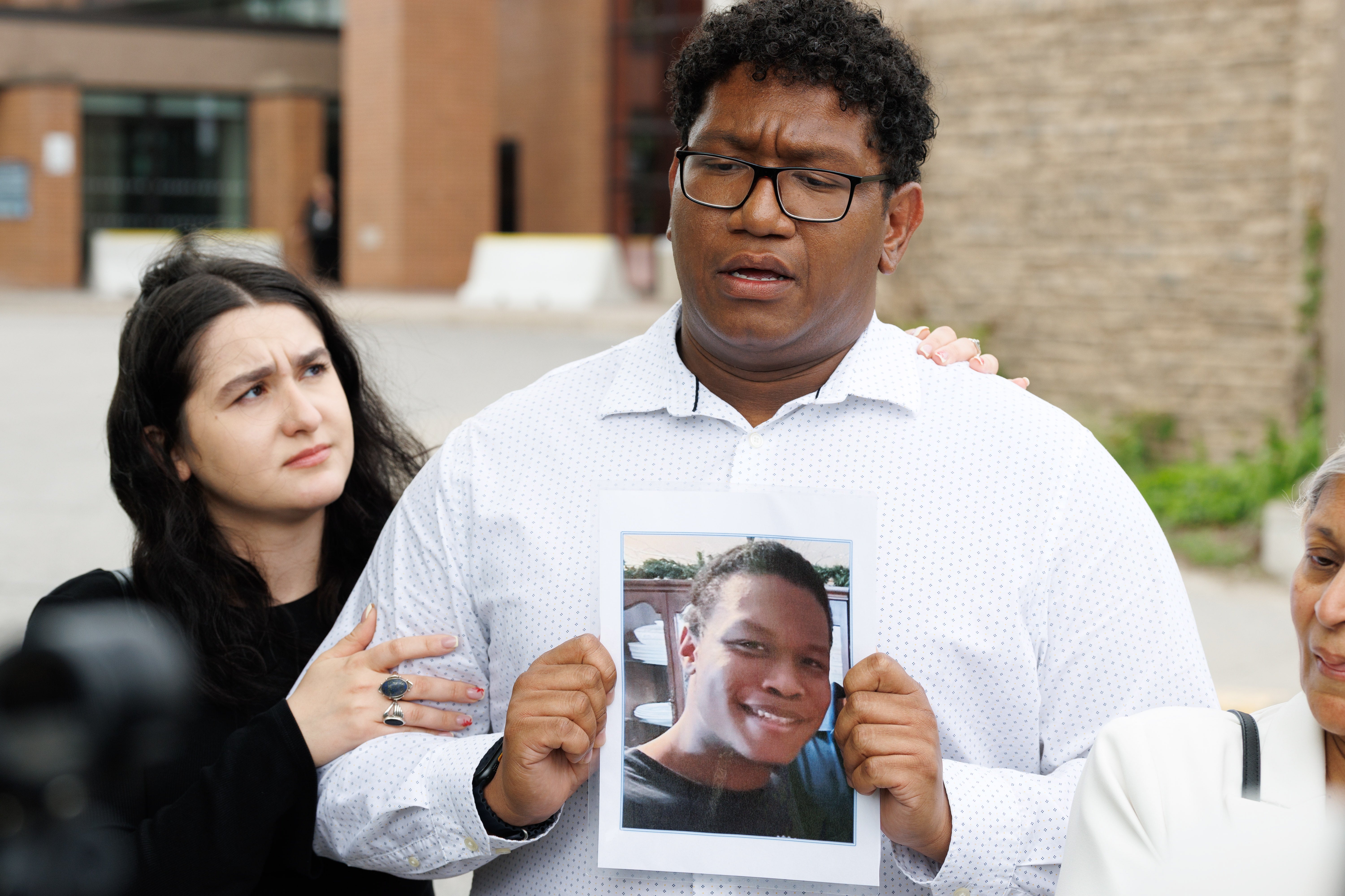 Ethan Mitchell holds a photograph of his brother, the late Stephen Mitchell Jr., as his partner Elena Castors stands beside him outside the Ontario Court of Justice