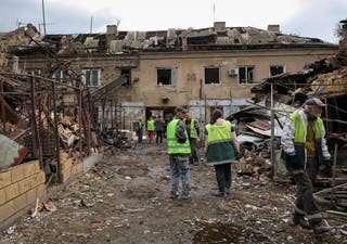 Communal workers stand at a site of an apartment building and houses damaged by a Russian drone strike