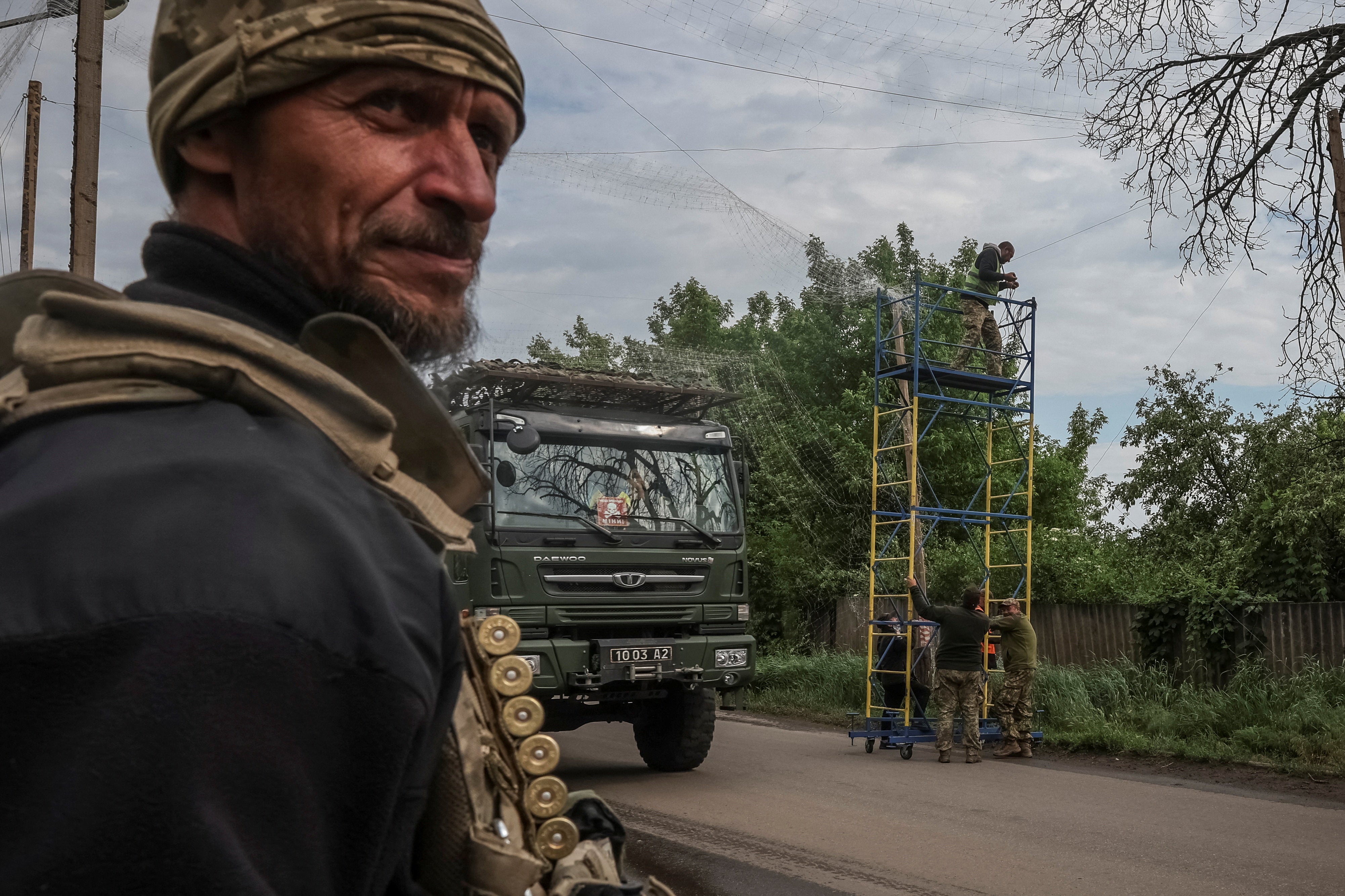 A military truck passes workers and service members installing anti-drone nets over a road in Donetsk region