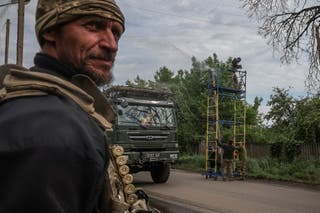 A military truck passes workers and service members installing anti-drone nets over a road in Donetsk region