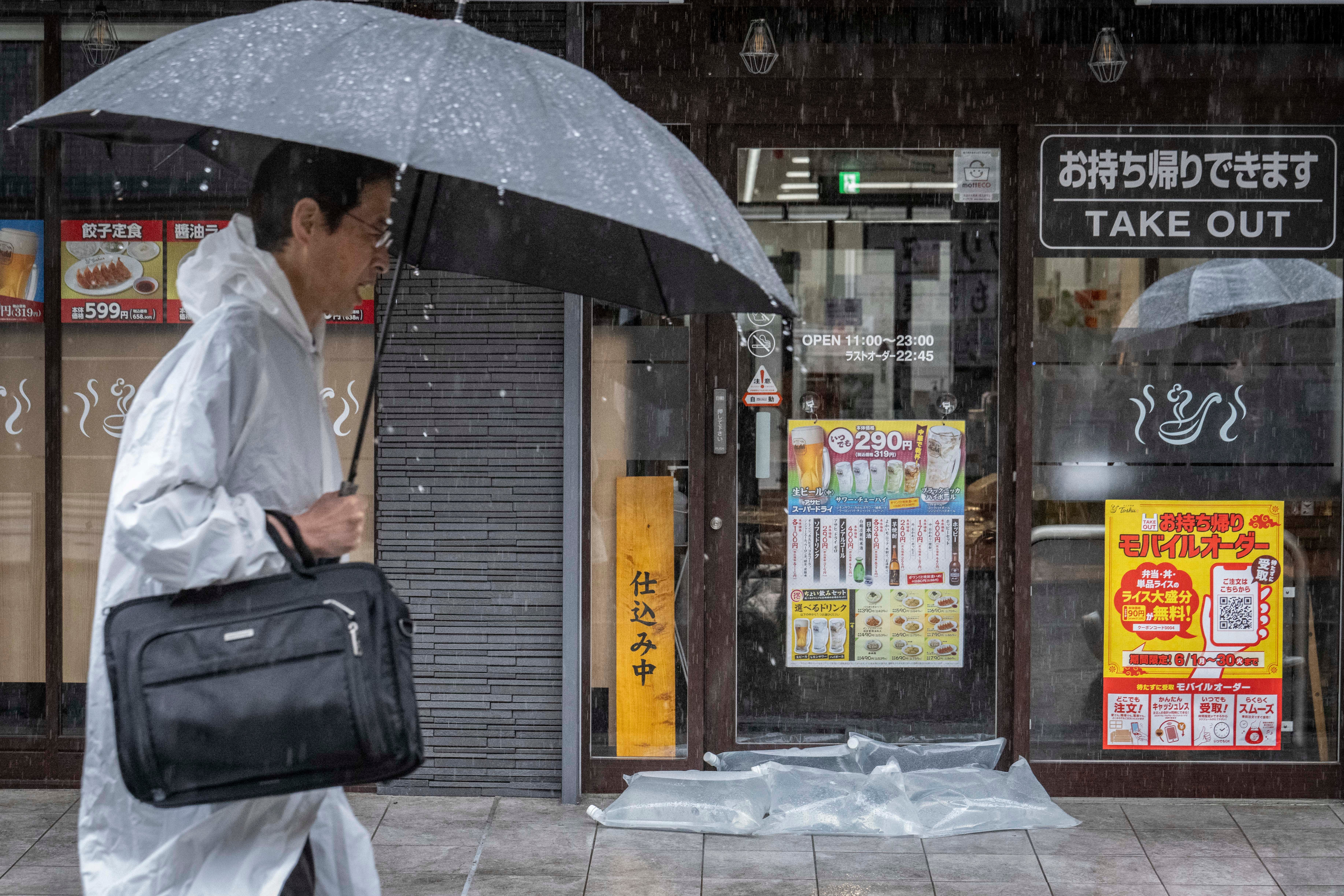 <p>Un hombre pasa frente a un restaurante donde colocaron sacos impermeables para evitar filtraciones, mientras las fuertes lluvias provocadas por la tormenta tropical severa Jangmi azotan Kawasaki, en la prefectura de Kanagawa, el 3 de junio de 2026  </p>