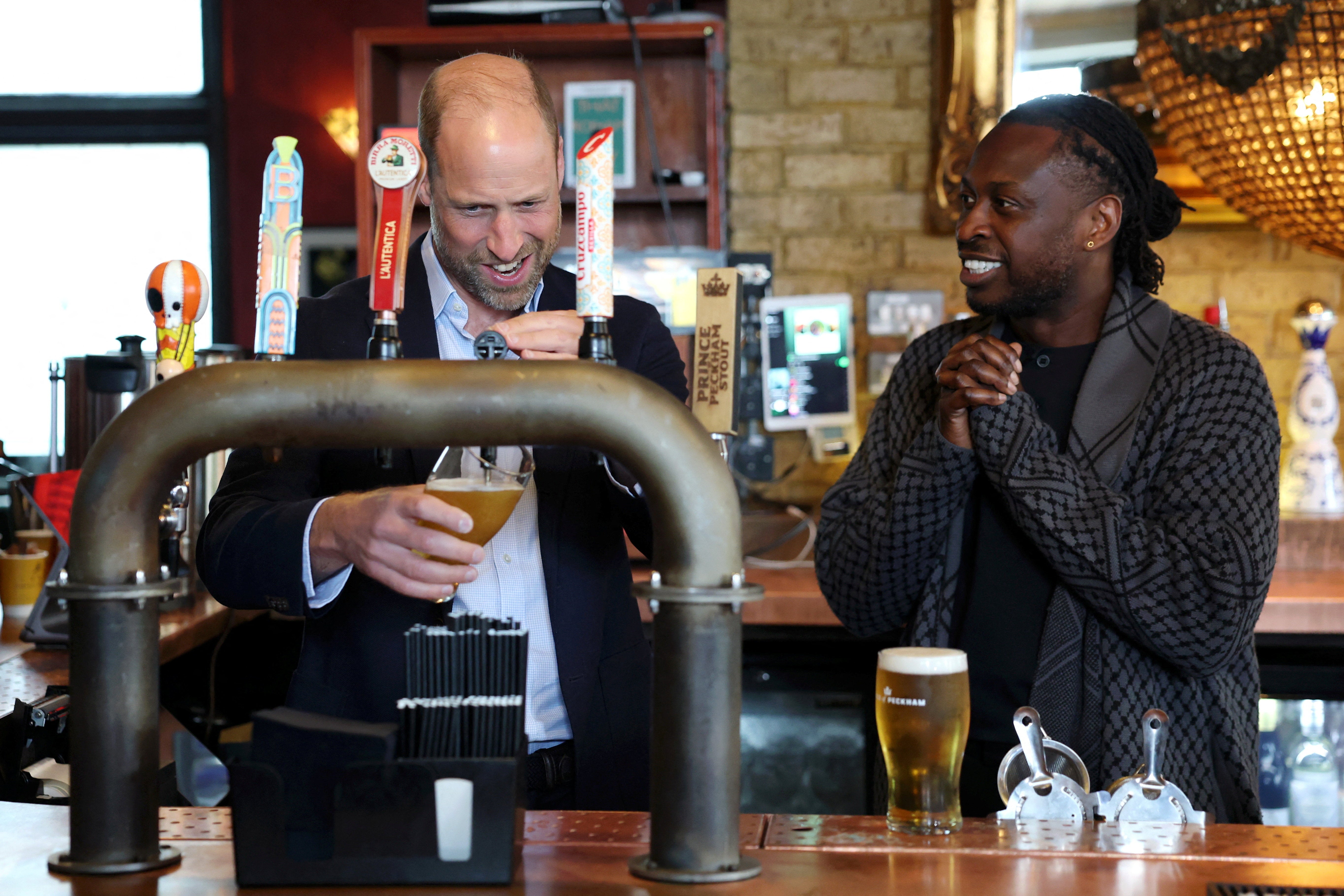 Prince William, Prince of Wales pours a pint alongside Clement Ogbonnaya during his visit to The Prince of Peckham pub