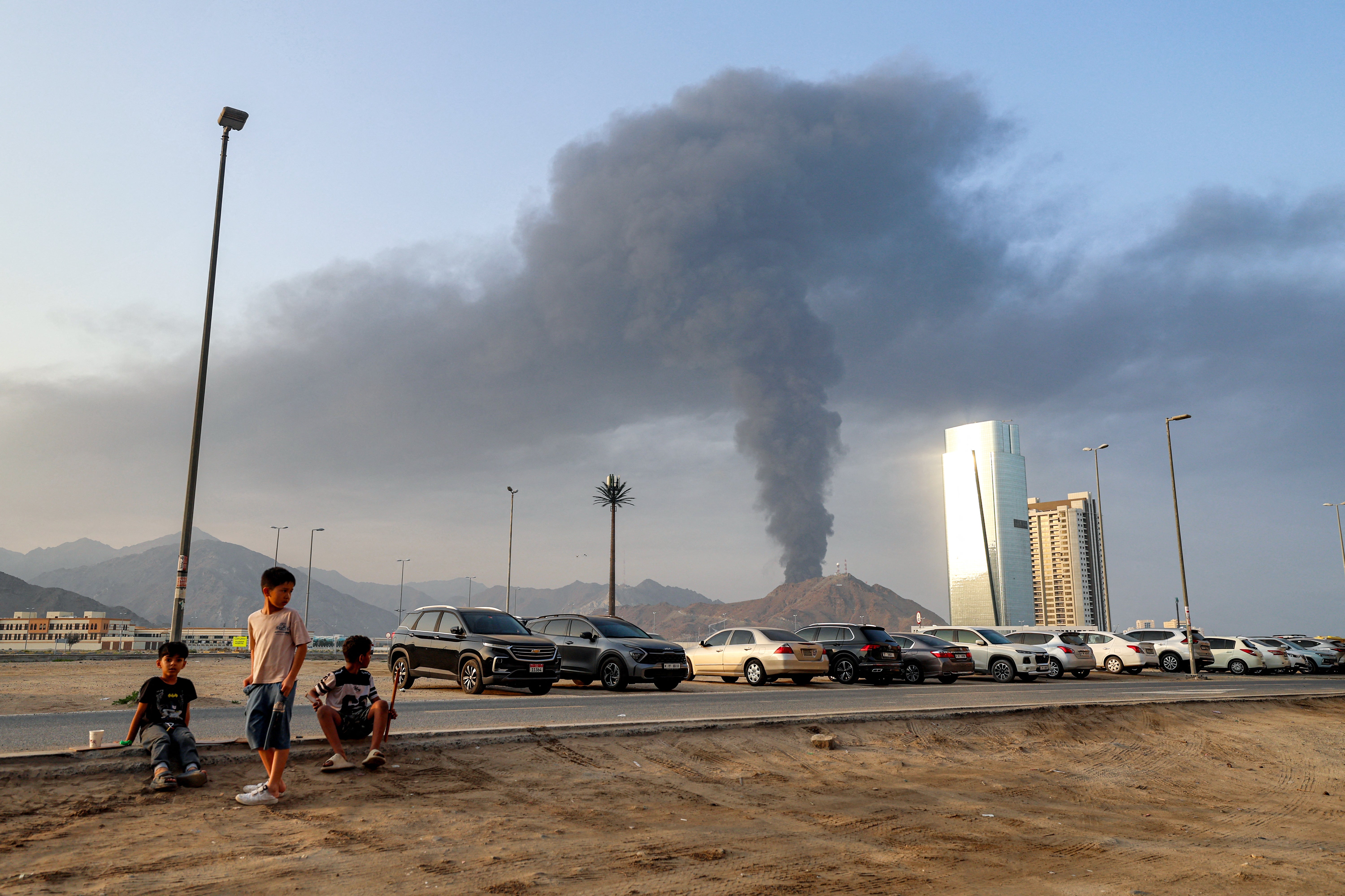Boys sit on the side of a road watch as a tall smoke plume billows following an explosion in the Fujairah industrial zone in the UAE earlier this year