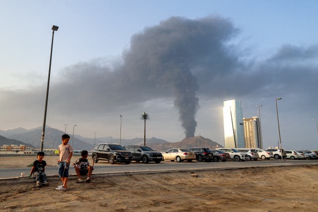 Boys sit on the side of a road watch as a tall smoke plume billows following an explosion in the Fujairah industrial zone in the UAE earlier this year
