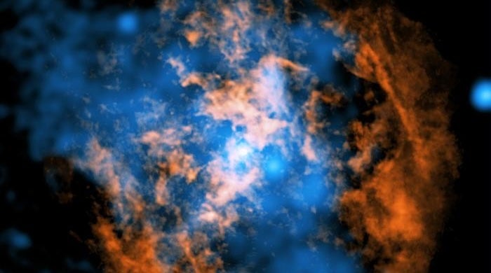 Astronomers say they’ve solved a longstanding mystery about Sagittarius A*, the supermassive black hole in the center of our galaxy. The white dot in the center of this composite image shows the black hole, the orange and blue areas mark surrounding gas and X-ray data and a cone-shaped cavity seen in the orange data is the key to their findings