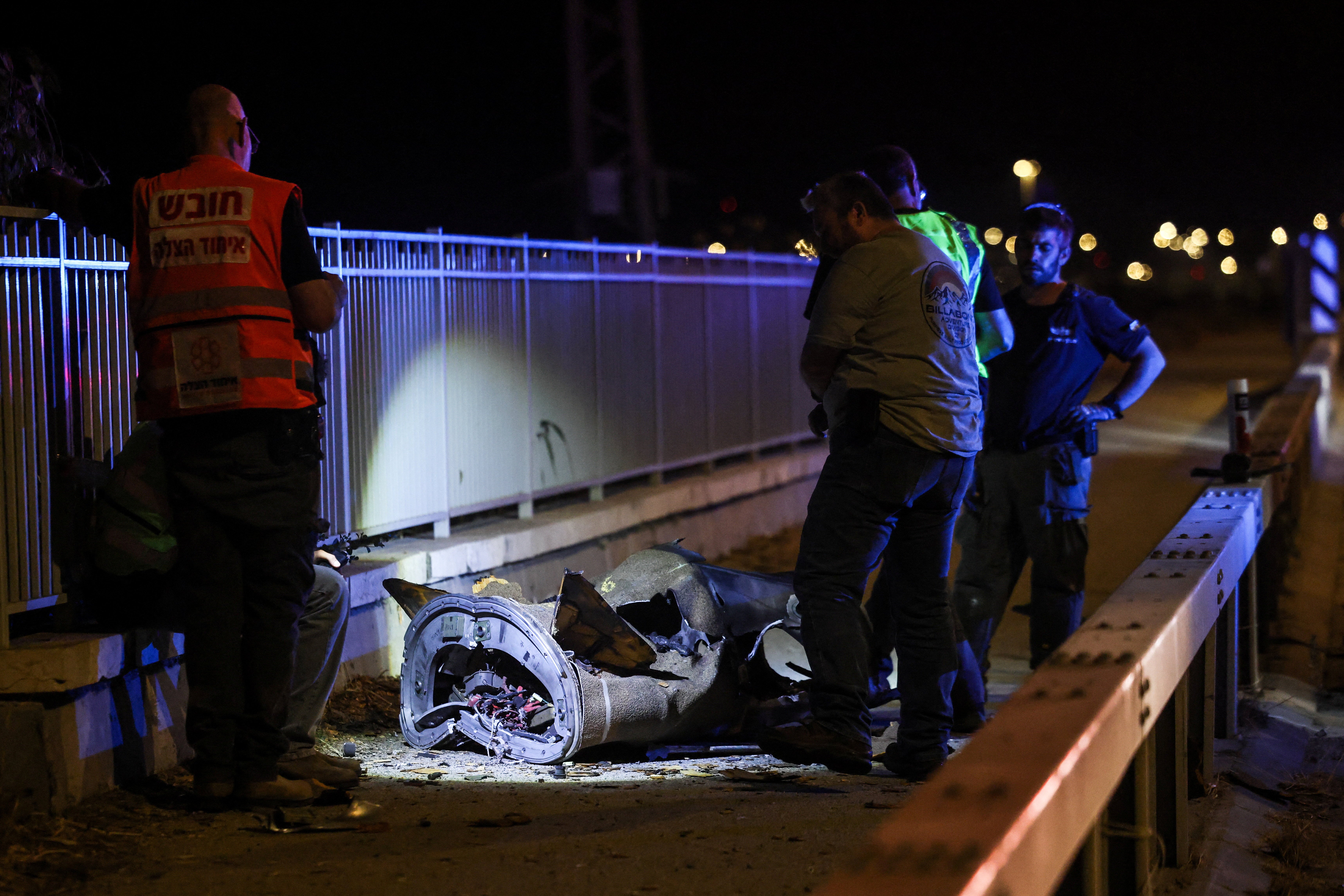 Israeli security and rescue personnel work next to a part of a projectile following a missile attack, June 8