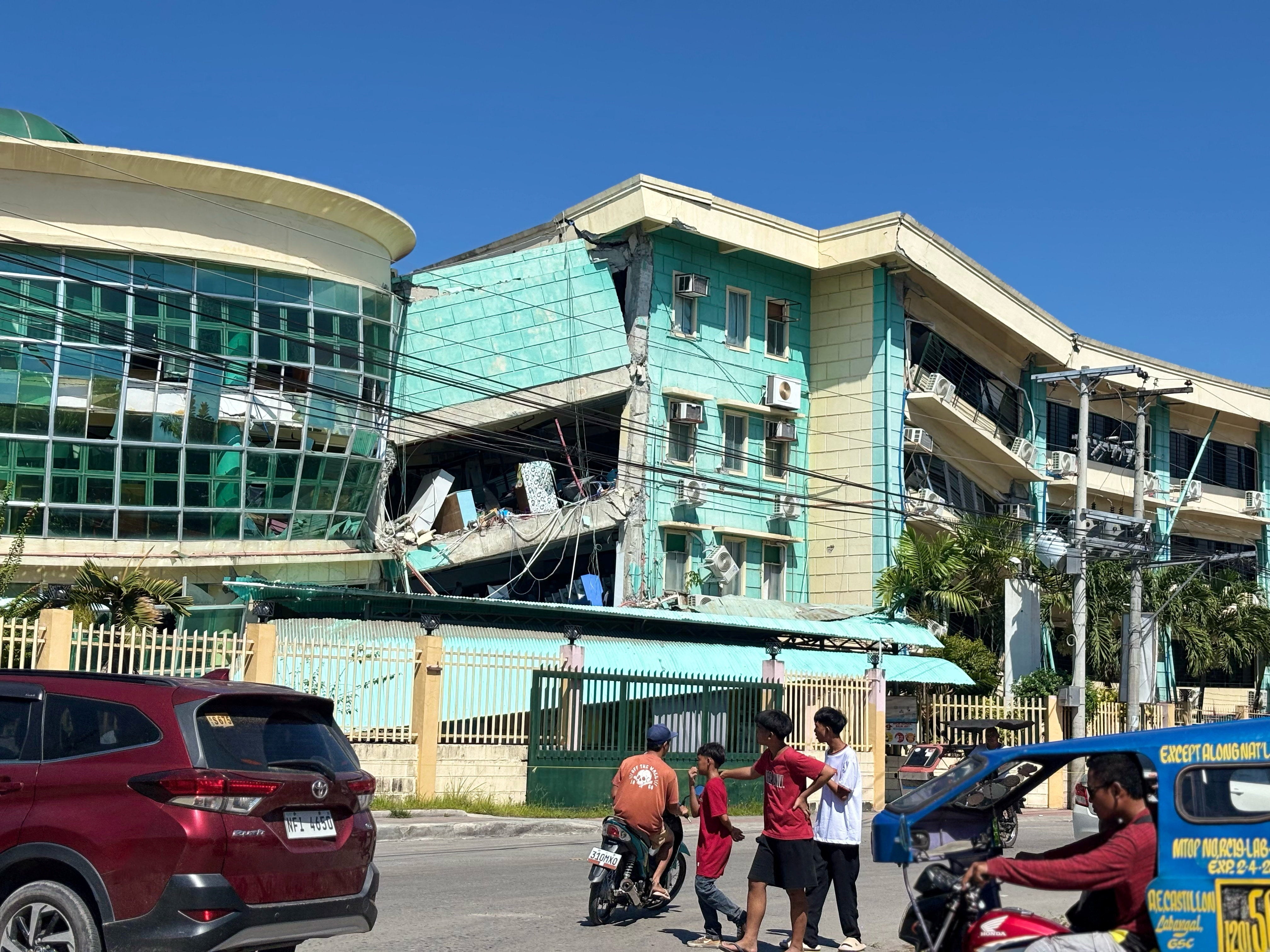 People move near damaged buildings after a magnitude 7.8 quake in General Santos, Mindanao Island, Philippines