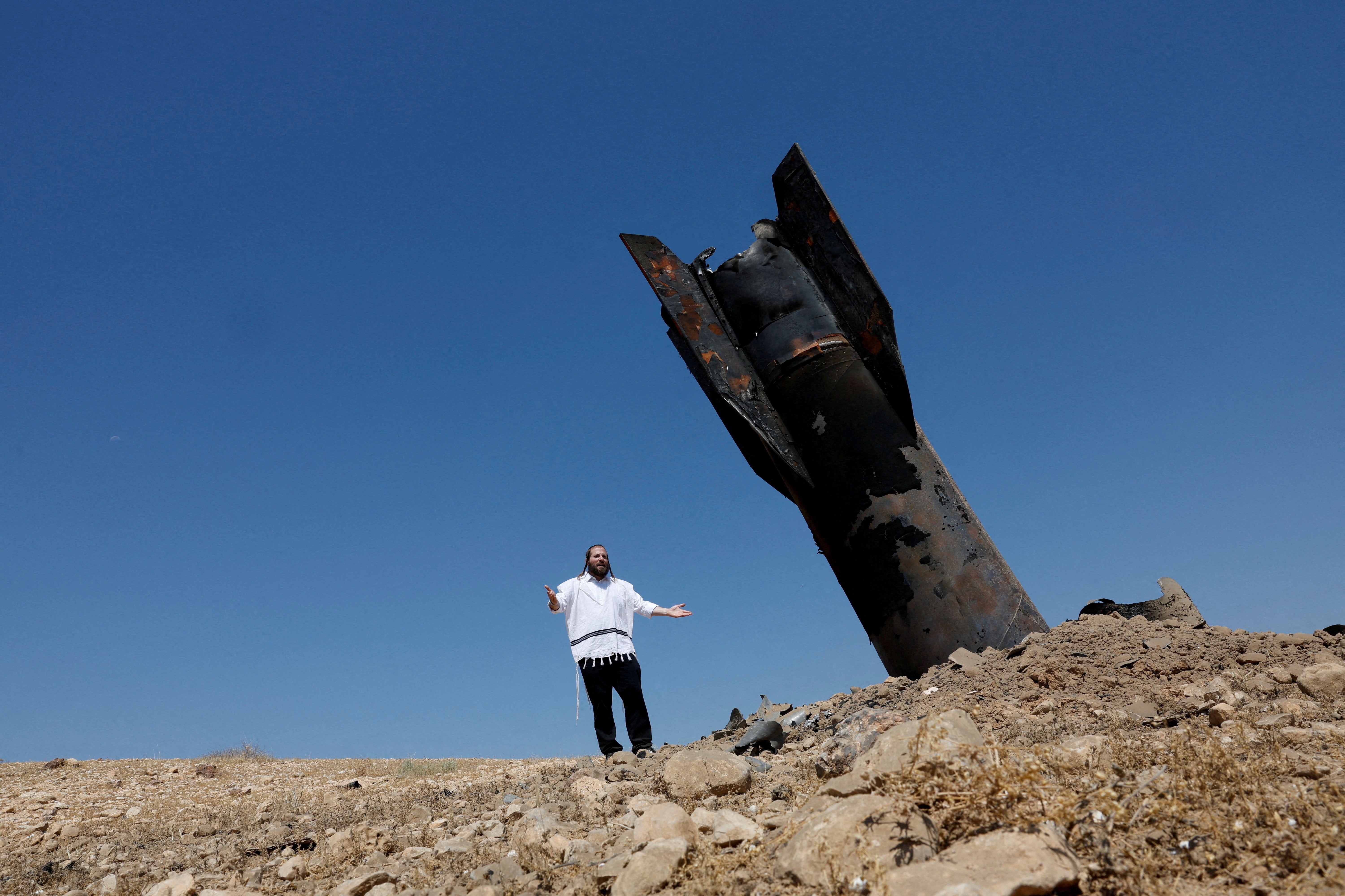 An Israeli settler stands near a part of a missile protruding from the ground, following strikes from Iran, in the central Israeli-occupied West Bank