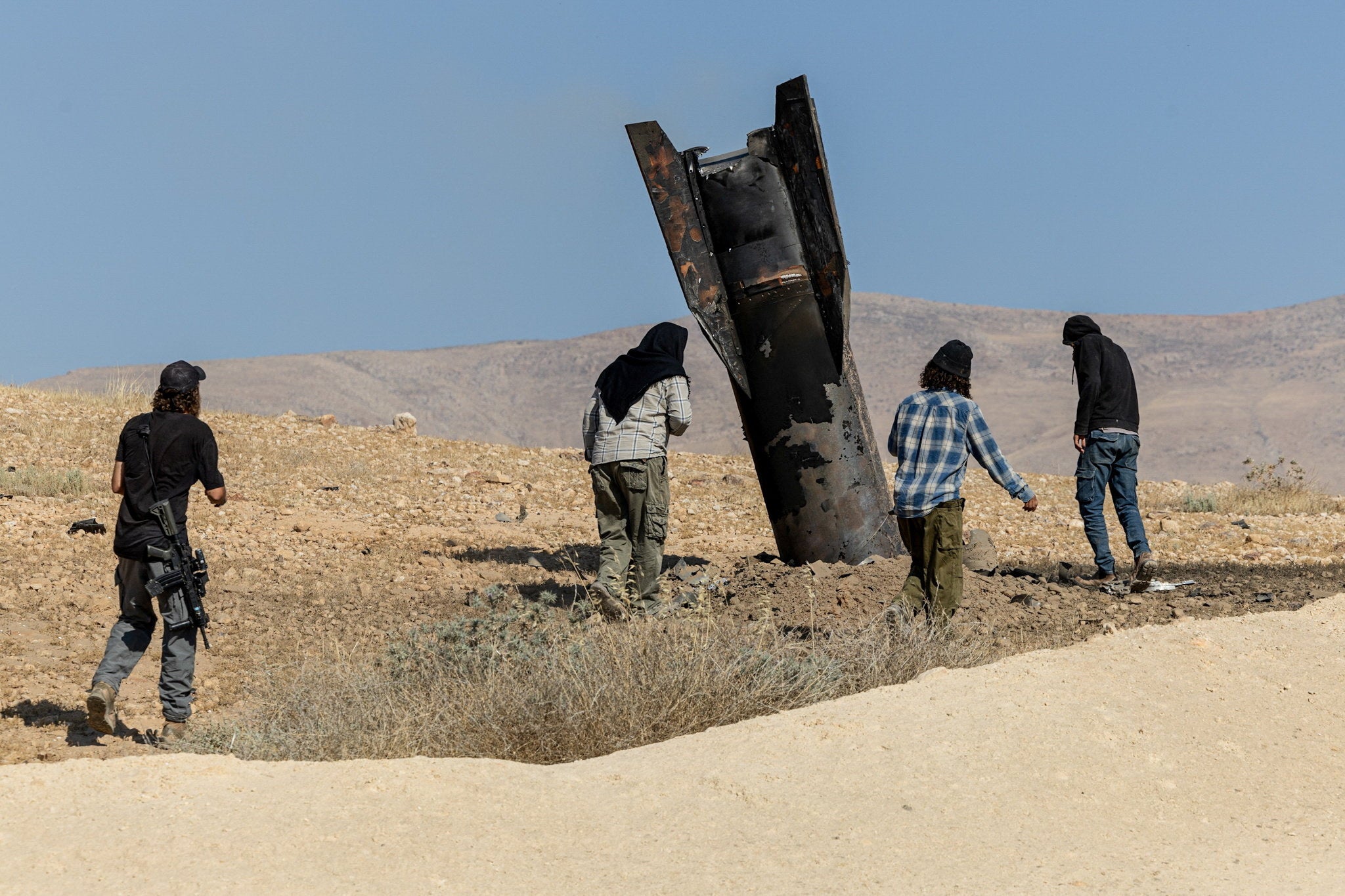 Israeli settlers stand next to part of a missile protruding from the ground, following strikes from Iran, in the central Israeli-occupied West Bank, 8 June 2026