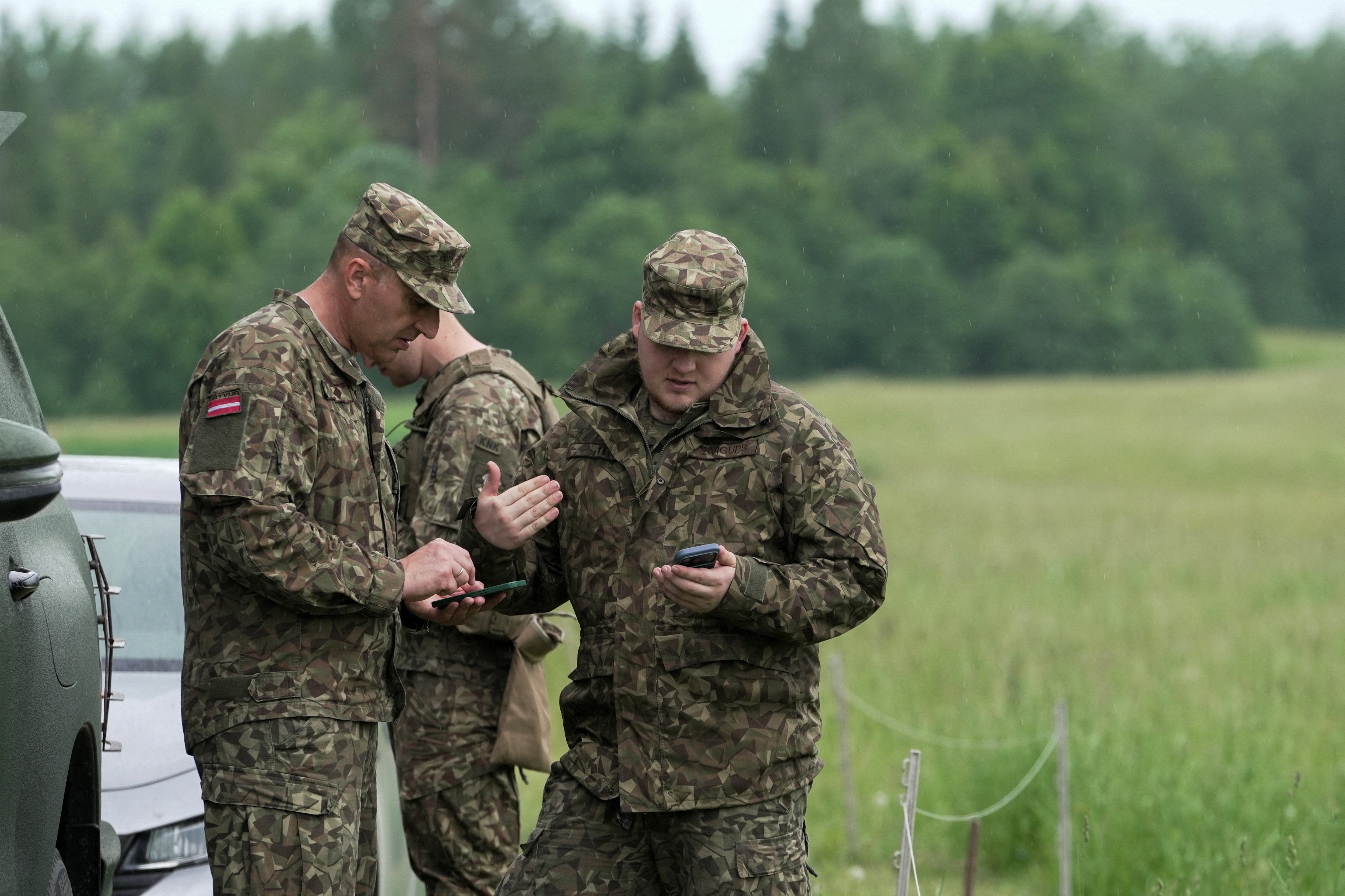 Servicemen of the Latvian National Guard look at phones as they search for the debris from an intercepted drone (Reuters)