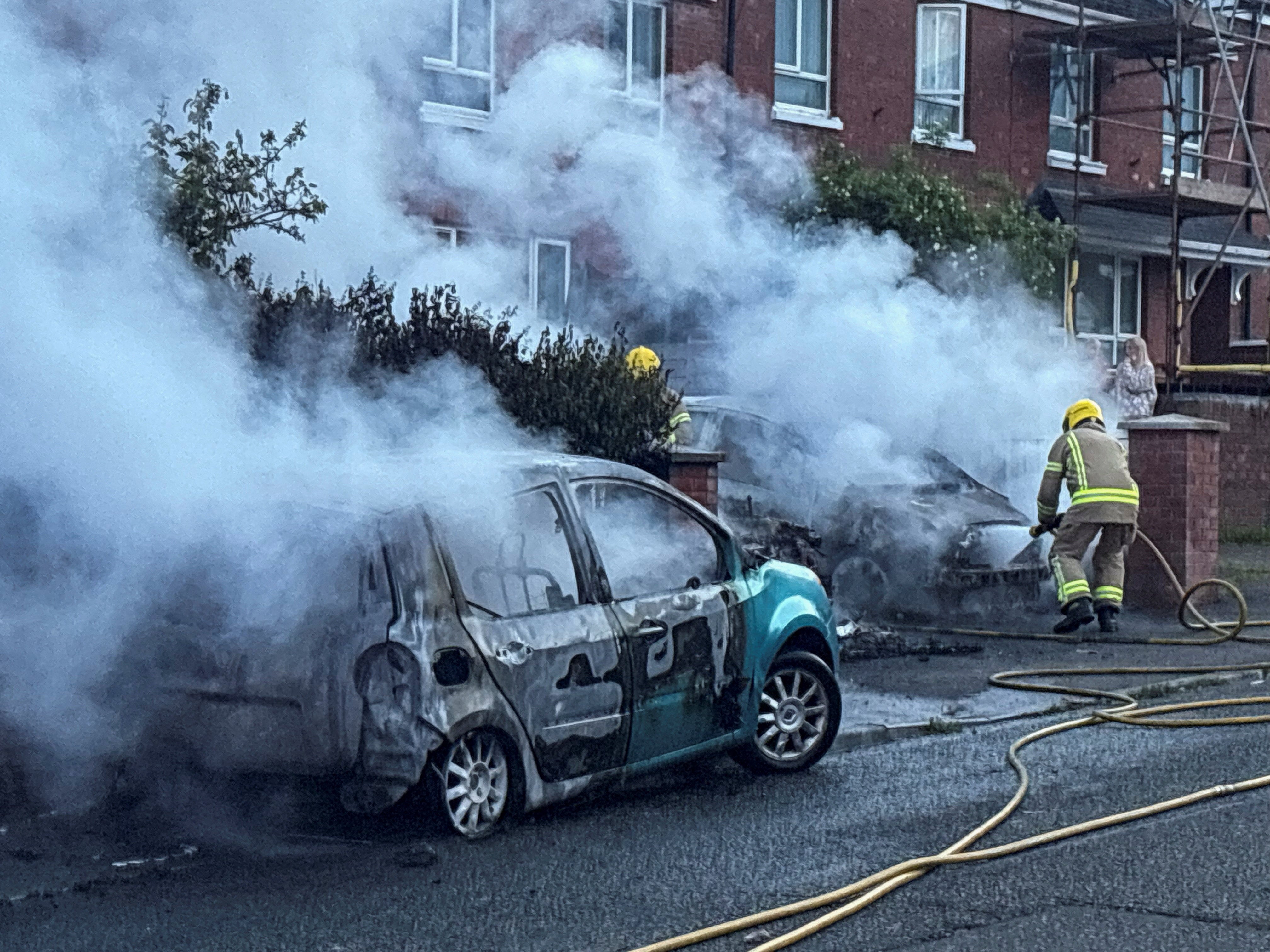 Firefighters work to extinguish a fire in three cars parked on the street at Tigers Bay