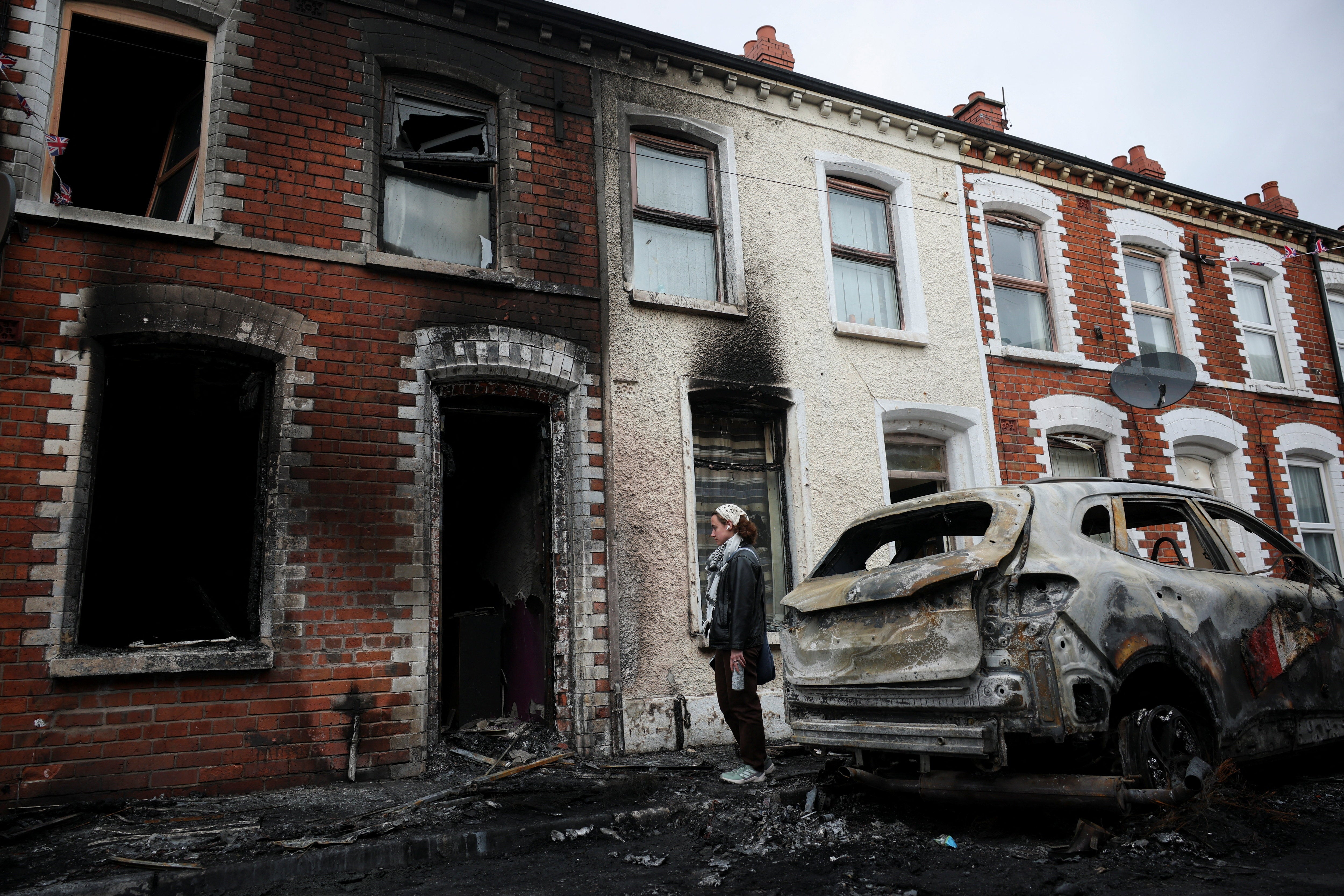 A resident looks at the charred debris scattered on the street in her neighbourhood, in the aftermath of anti-immigrant protests