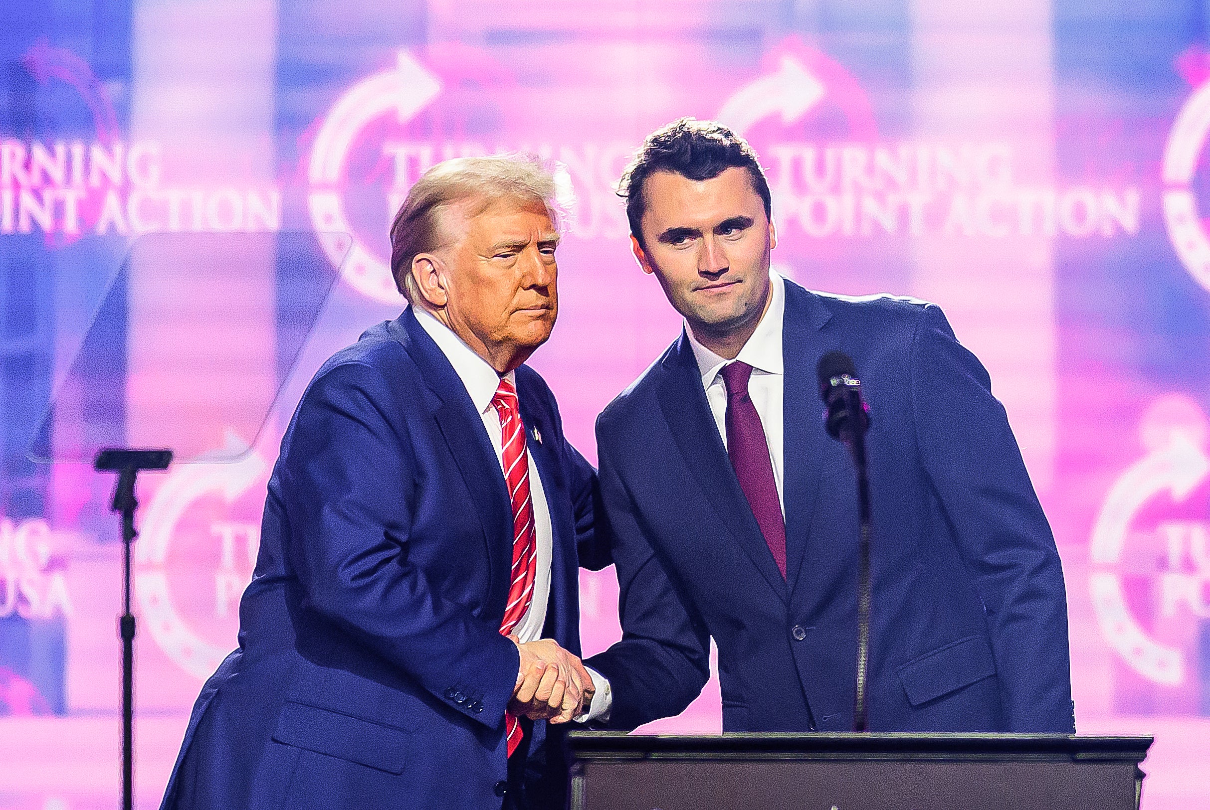This photo taken on December 22, 2024 shows right-wing activist Charlie Kirk (R) shaking hands with US President Donald Trump as he speaks on stage at America Fest 2024 in Phoenix
