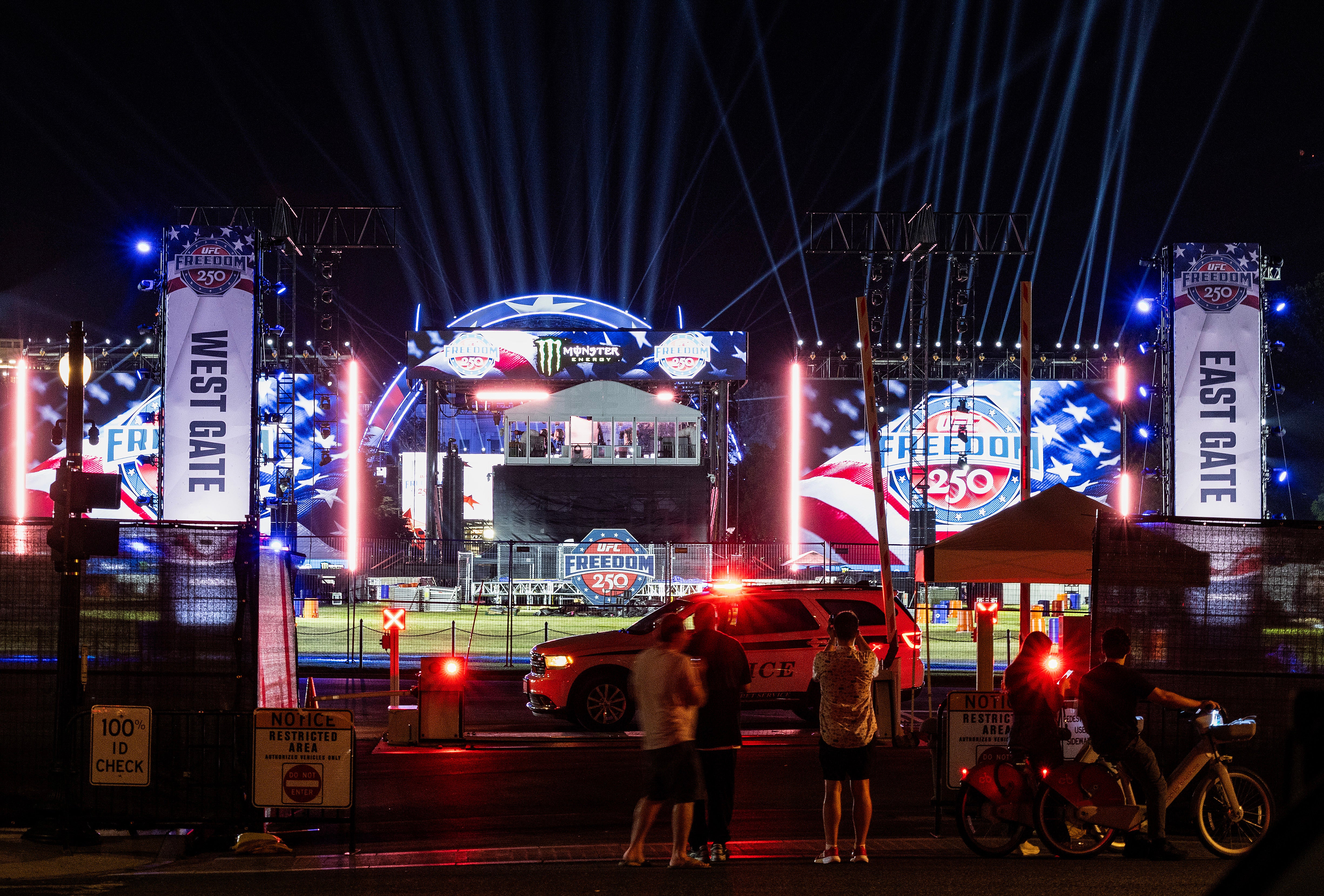 People stop to look and take pictures as stage lights are tested for the upcoming Ultimate Fighting Championship Freedom 250 event on the South Lawn of the White House