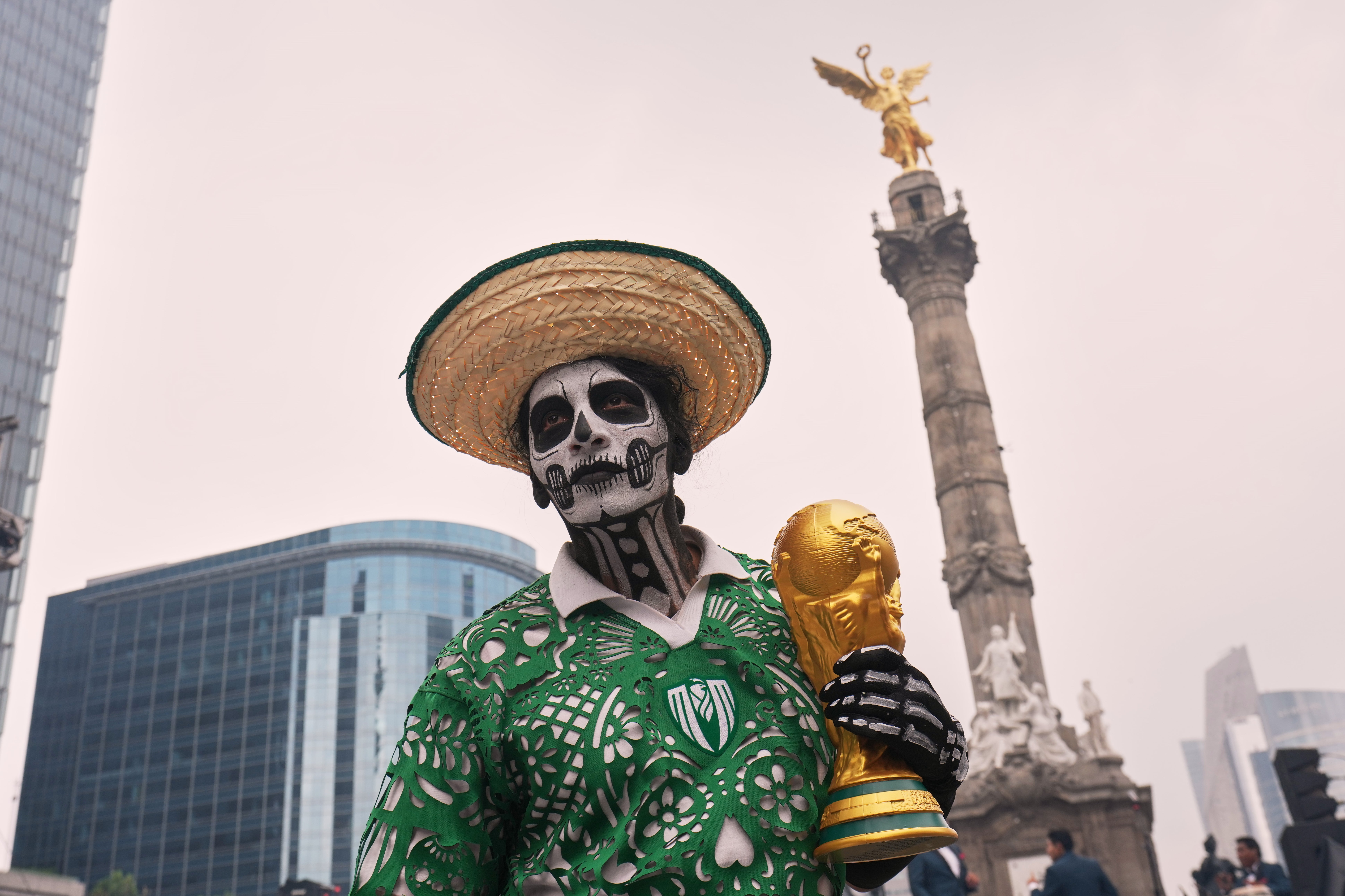 A dancer holds a replica of the World Cup trophy as soccer fans stand along Reforma Avenue in Mexico City