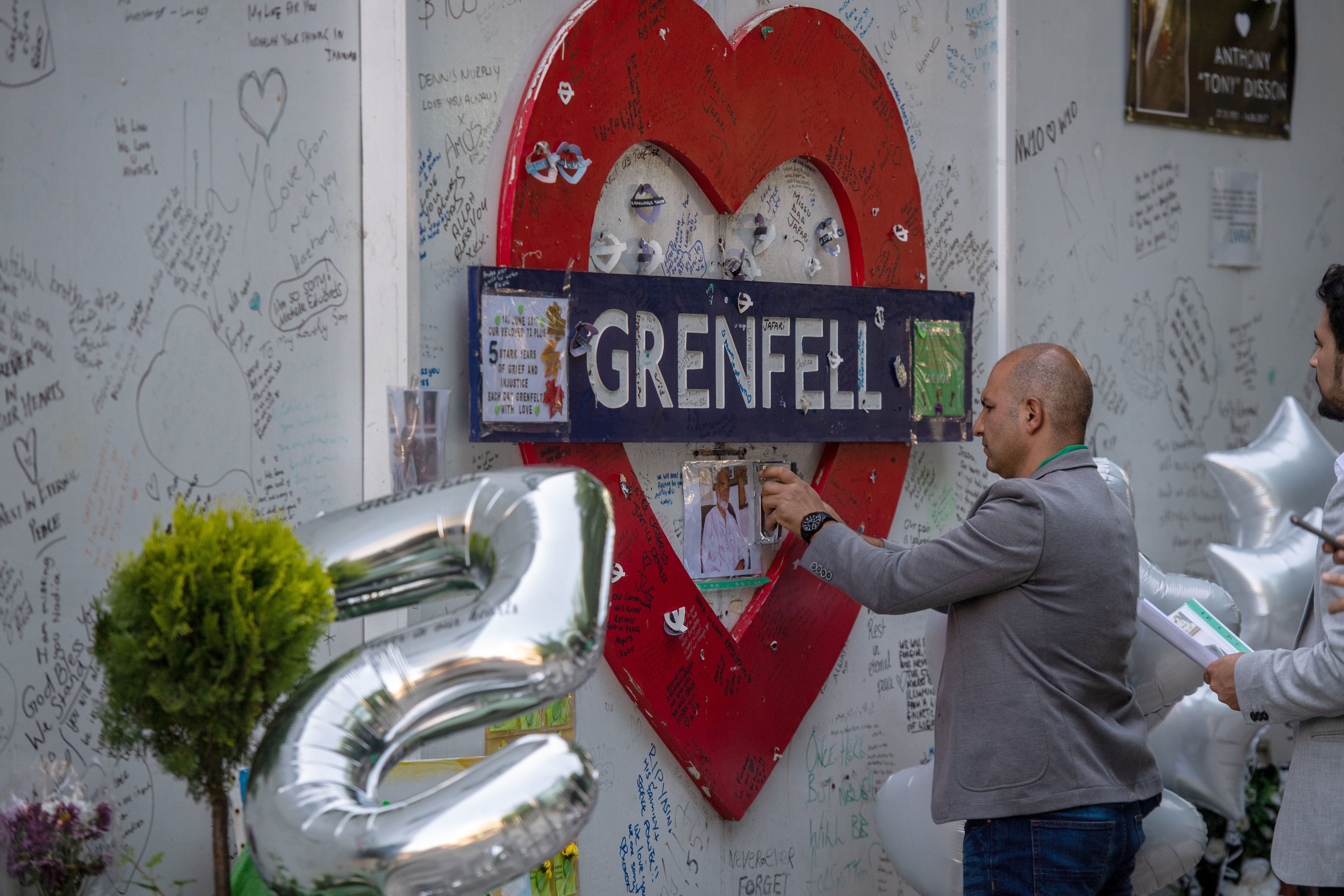Hamid Ali Jafari staples his father Ali Yawar Jafari's photo in 2022 to the memorial wall at Grenfell Tower