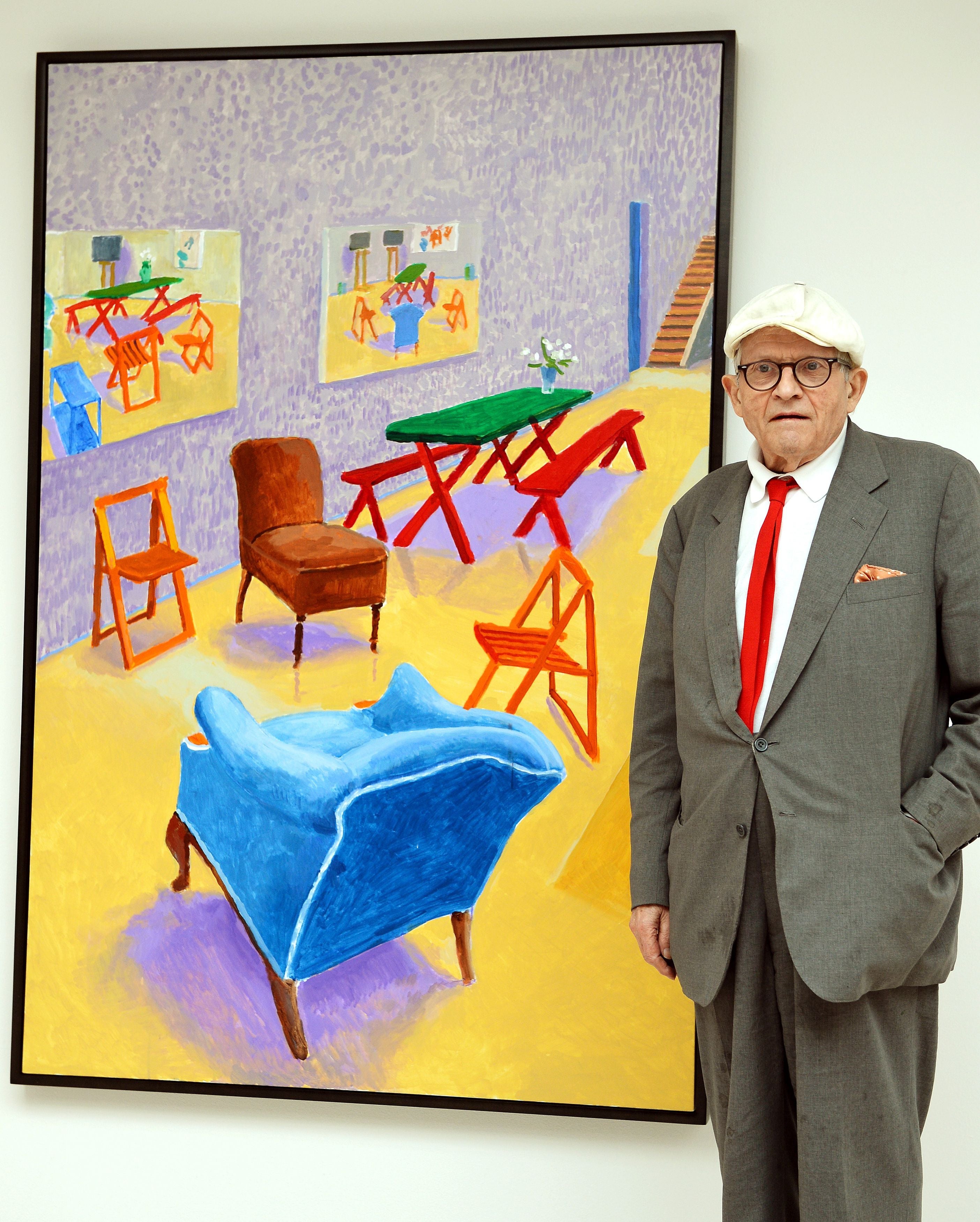David Hockney standing with his work, “Studio Interior #2” in 2015