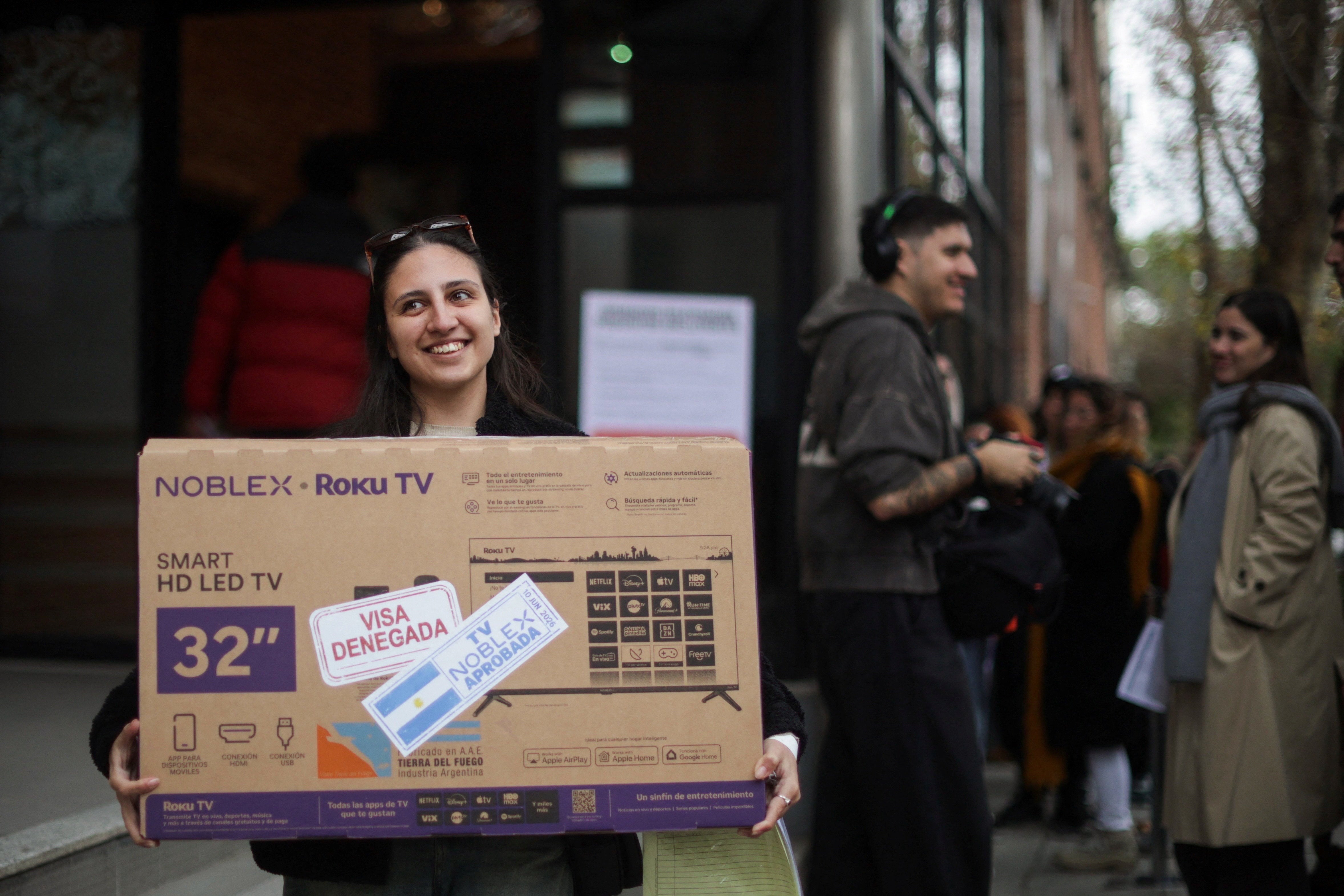 A woman carries a television set she received for free after showing her U.S. visa denial during a promotion by television manufacturer Noblex for people unable to travel to the World Cup due to visa rejections, in Buenos Aires, Argentina