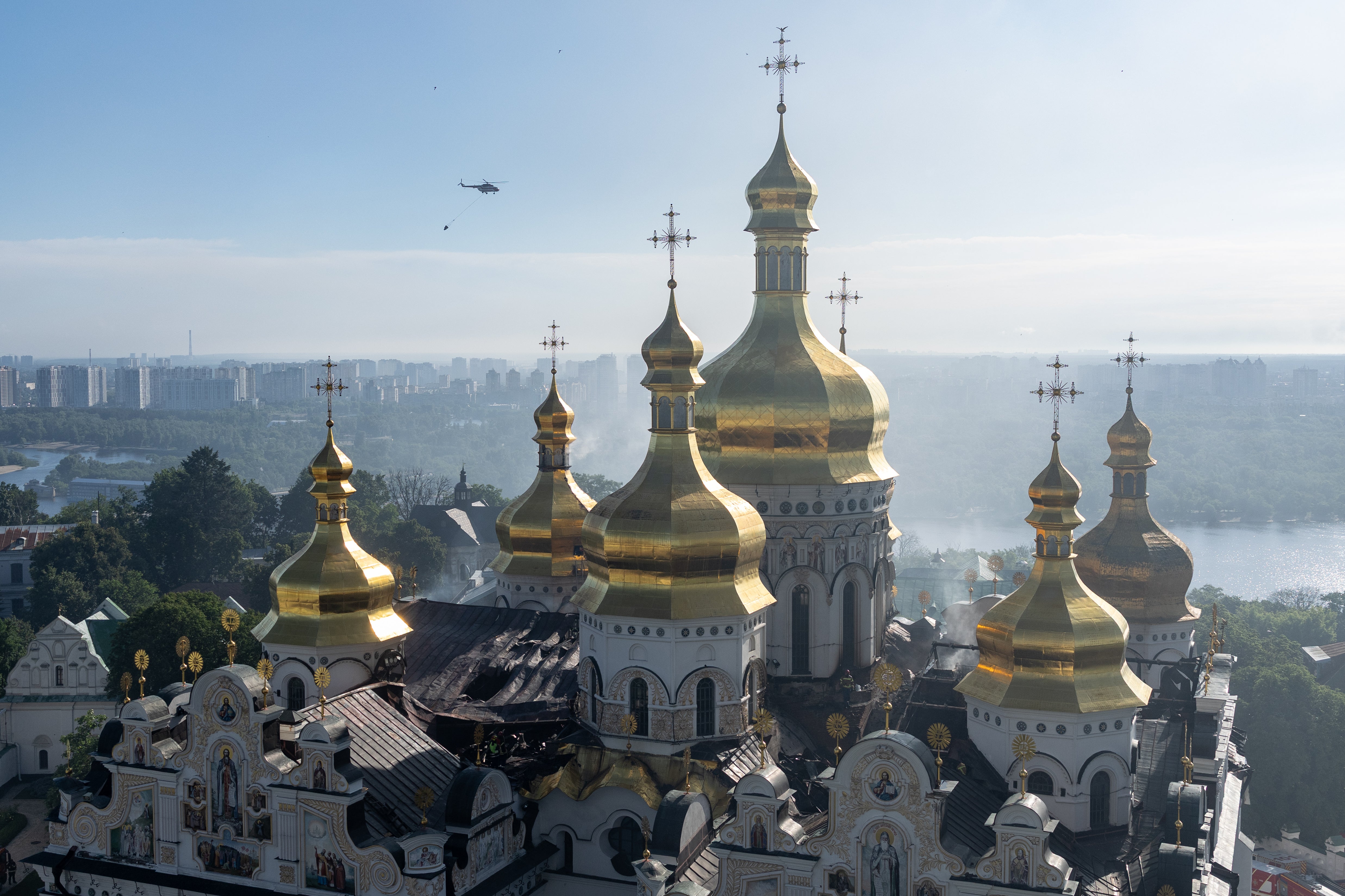 Firefighters work to extinguish a fire on the damaged roof of the Dormition Cathedral in the Orthodox complex of the Kyiv Pechersk Lavra as a helicopter passes by following a Russian missile strike (Getty)