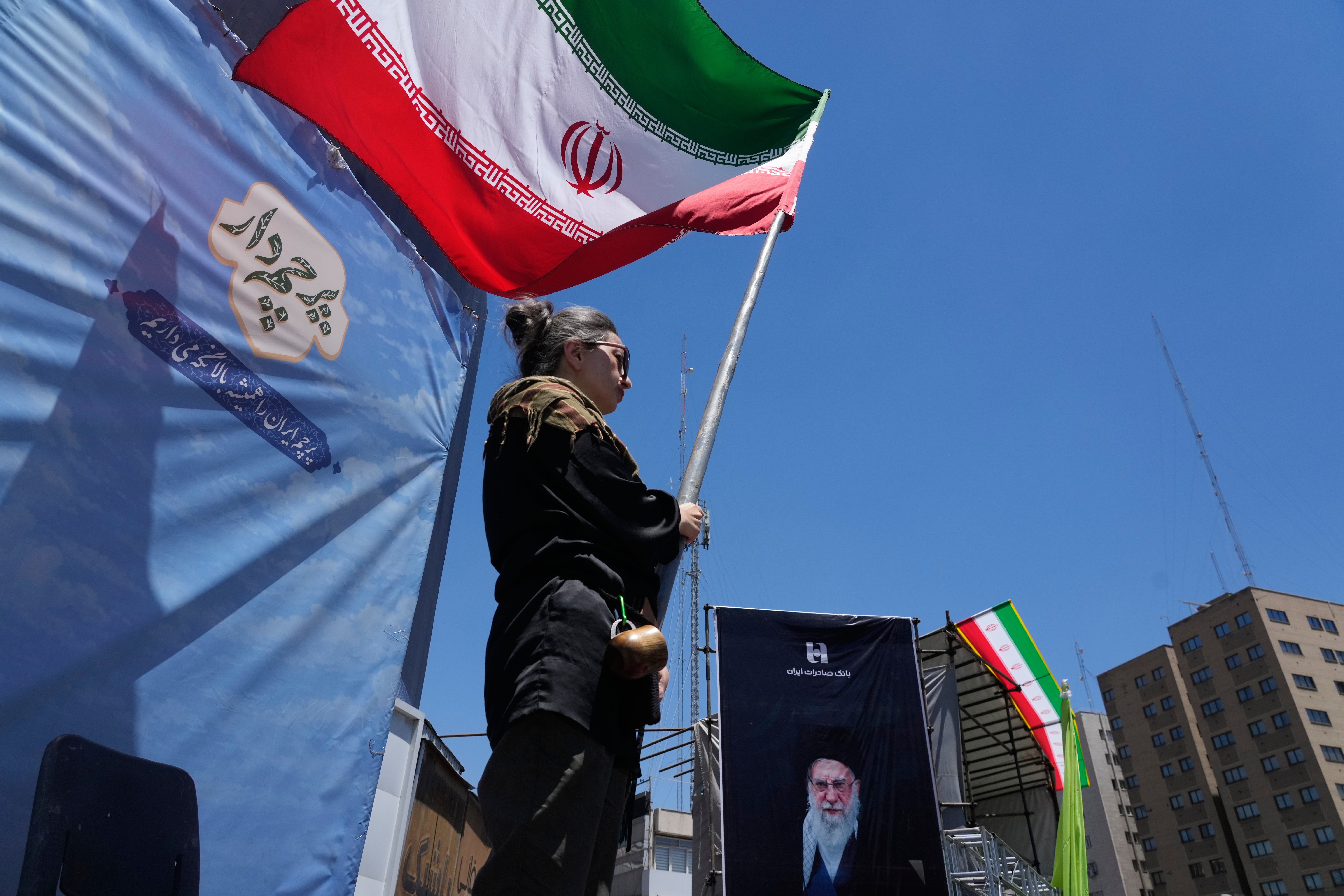A woman waves an Iranian flag during a pro-government campaign as a portrait of the slain Supreme Leader Ayatollah Ali Khamenei, who was killed in U.S. and Israeli strikes on Feb. 28, is displayed at right, in downtown Tehran on Monday