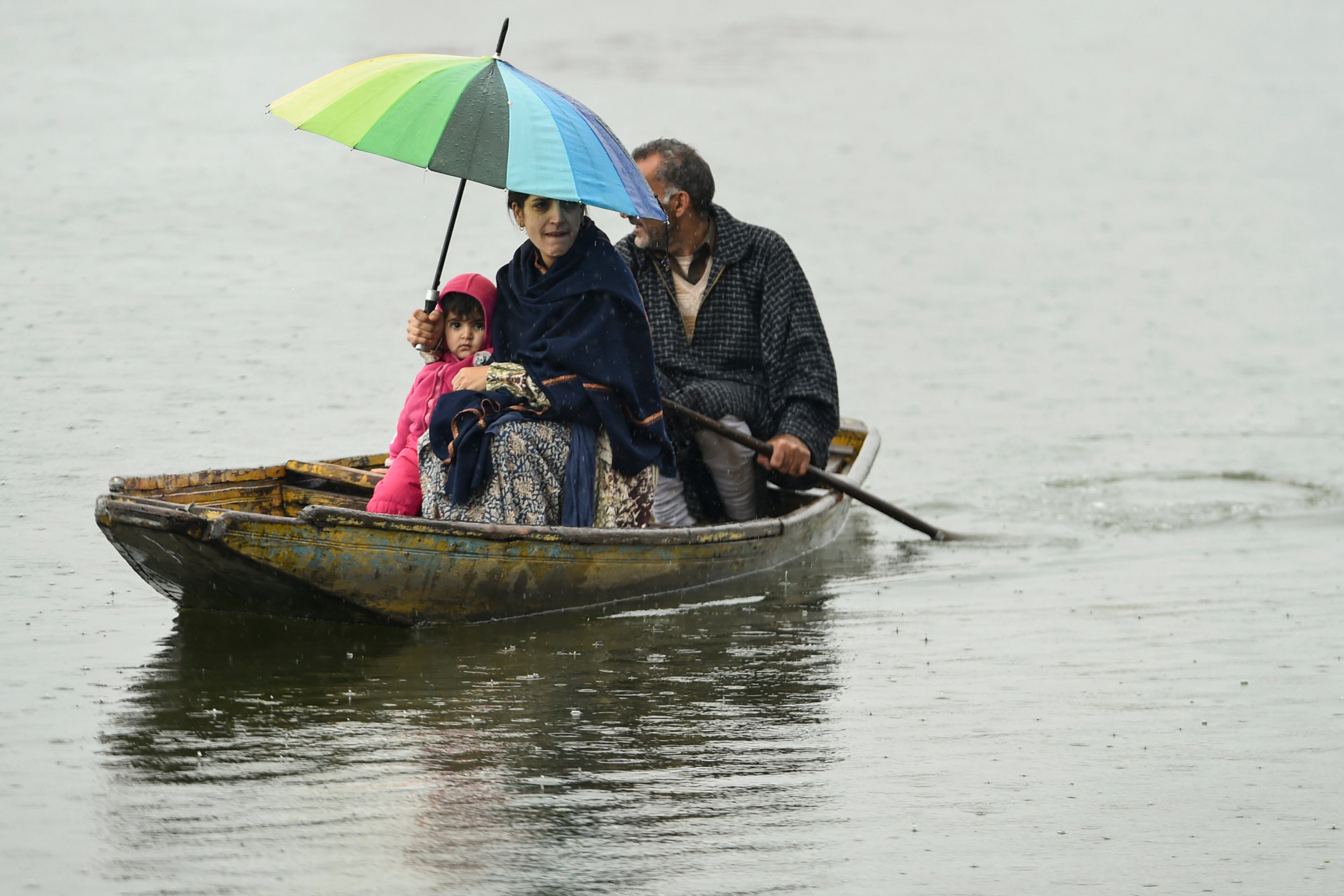 A Kashmiri woman shelters from the rain under an umbrella with a child while a man paddles a boat along Dal Lake in Srinagar