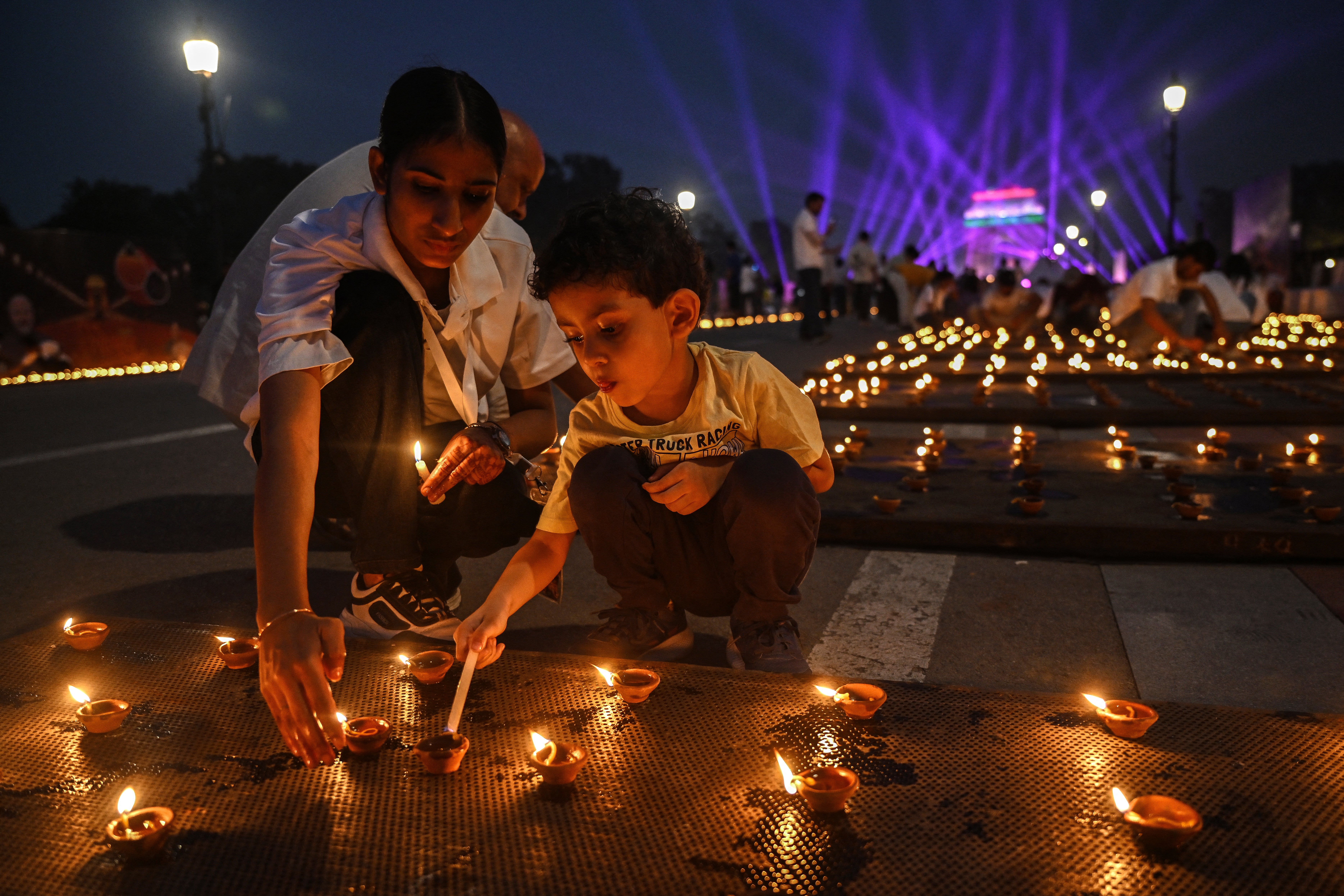 People light diyas, or traditional earthen oil lamps, as a drone laser show is organised at the India Gate memorial as part of the Diwali celebrations, the Hindu festival of lights, at Kartavya Path in New Delhi on 18 October 2025