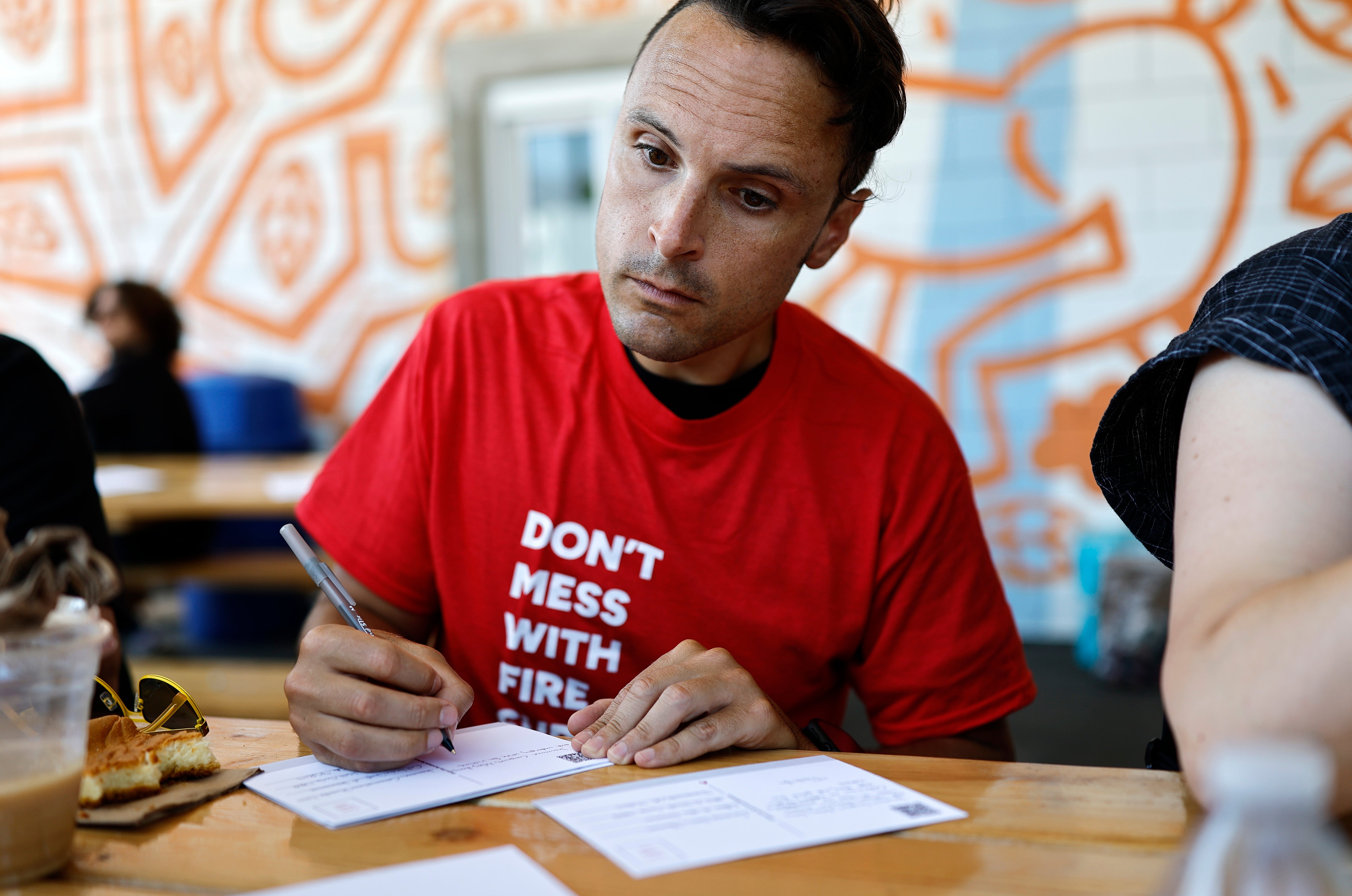 A man writes a postcard as part of a campaign by the Eaton Fire Survivors Network in Altadena, California, in July 2025. Writing by hand requires focus, intention and can be therapeutic