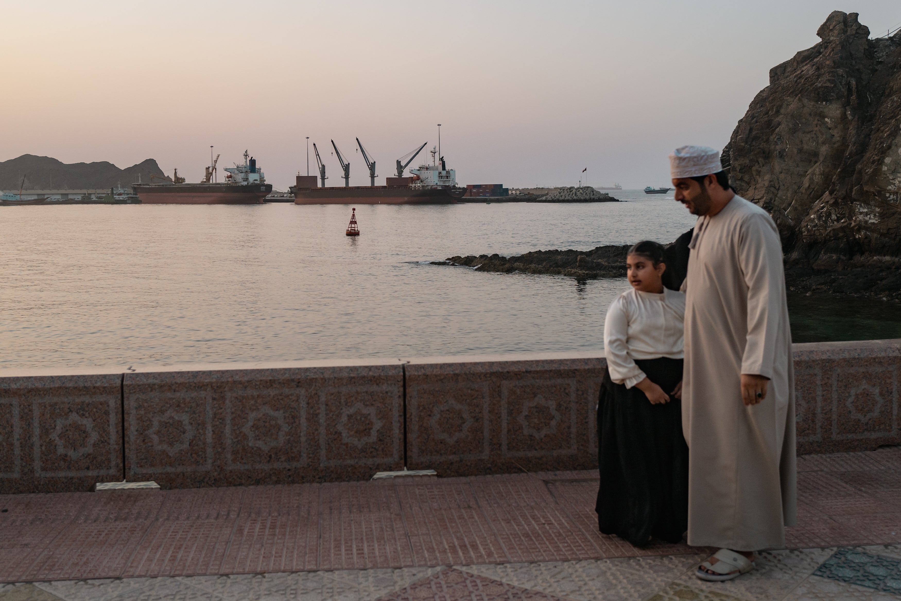 A family poses for pictures as oil tankers, general cargo ships, bulk carriers, and fishing boats sit anchored in the waters off Muscat near the Strait of Hormuz on 18 June 2026